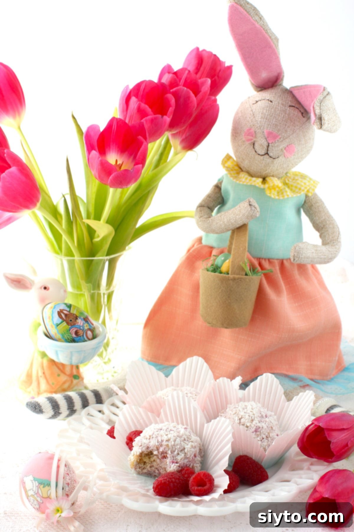 Raspberry Snowballs 12 Schneeballen on a plate, with vase of tulips behind and an Easter bunny.
