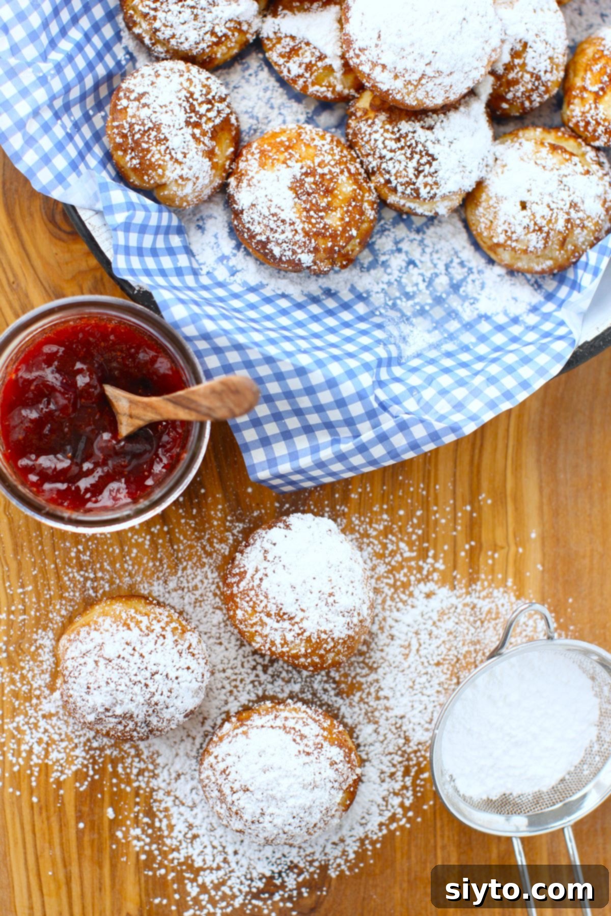 A charming top-down view displaying a plate of Aebleskiver, three additional ones on a cutting board, and a jar of homemade jam, set for a delightful serving.