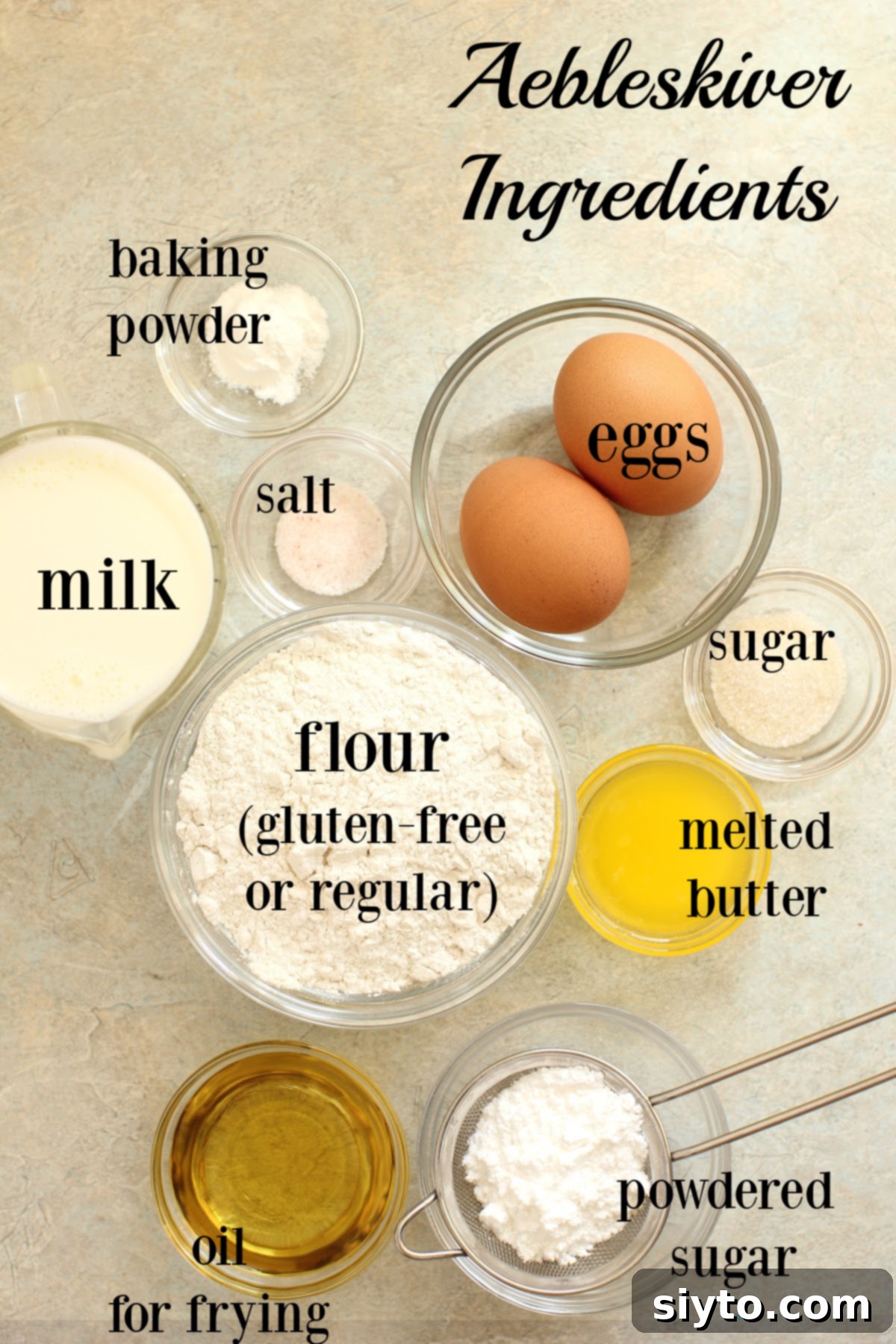 A collection of ingredients laid out for making Aebleskiver pancakes, including flour, eggs, milk, sugar, salt, baking powder, and butter.