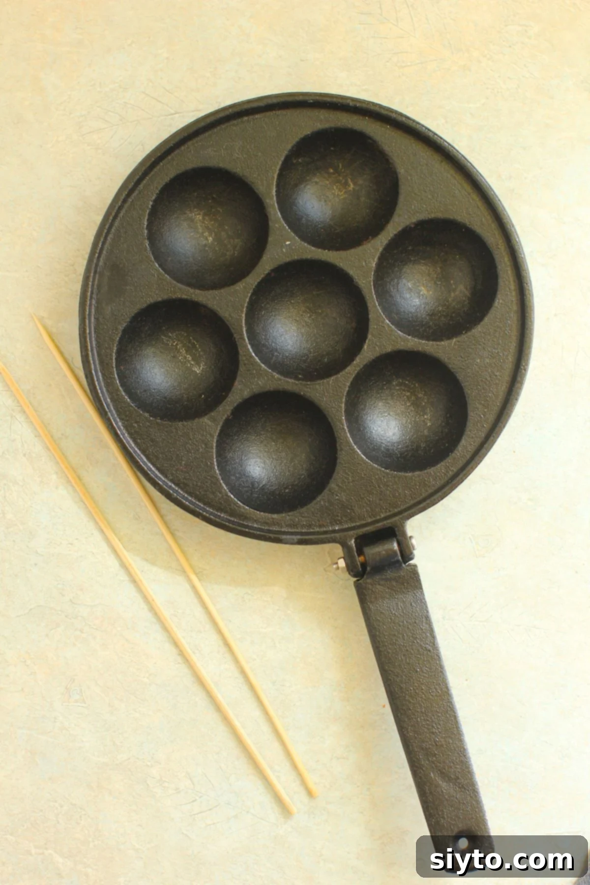 A traditional Aebleskiver pan, made of well-seasoned cast iron, positioned next to two slender bamboo skewers.