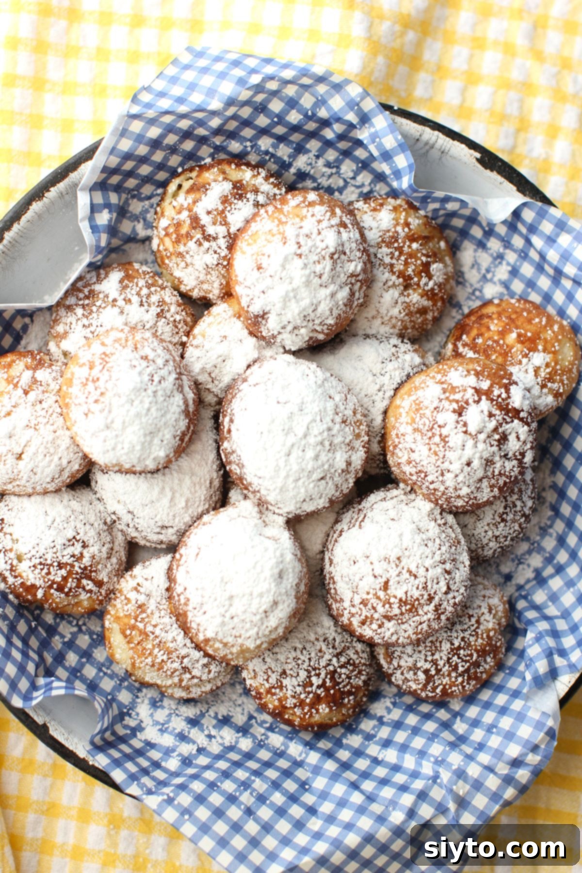 A top-down view of a plate of freshly made Aebleskiver, presented on a blue and white checked paper liner, ready for serving.