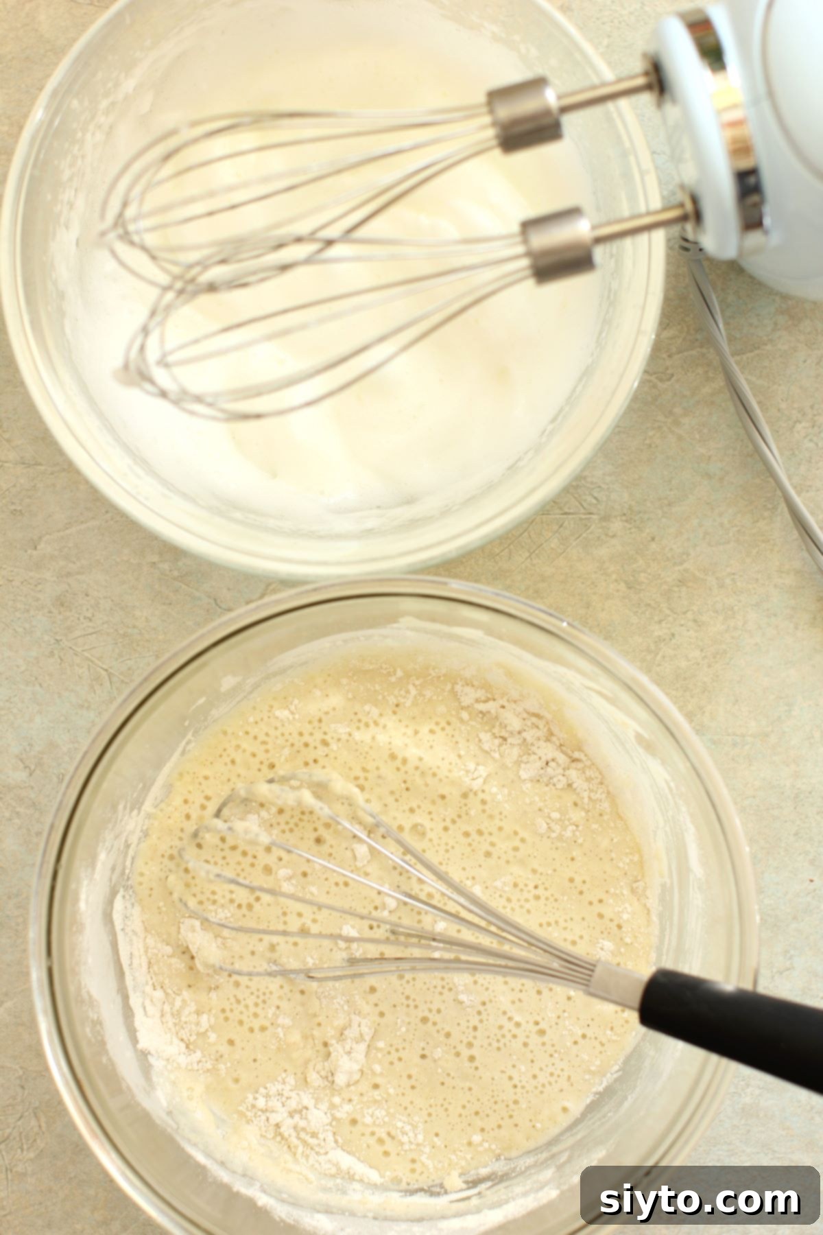 A two-bowl setup: one containing a smooth pancake batter and the other holding stiffly whipped egg whites, essential components for Aebleskiver.