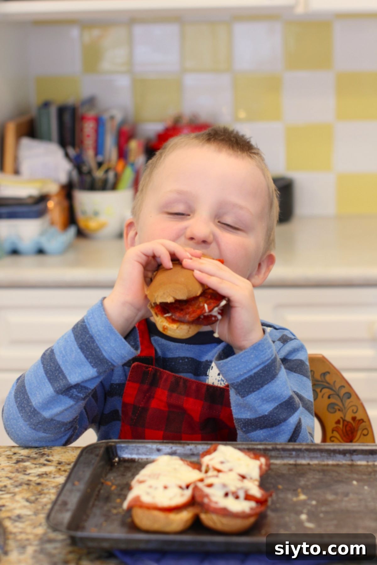 Caleb biting into a pizza dog with his eyes closed, showing immense pleasure.