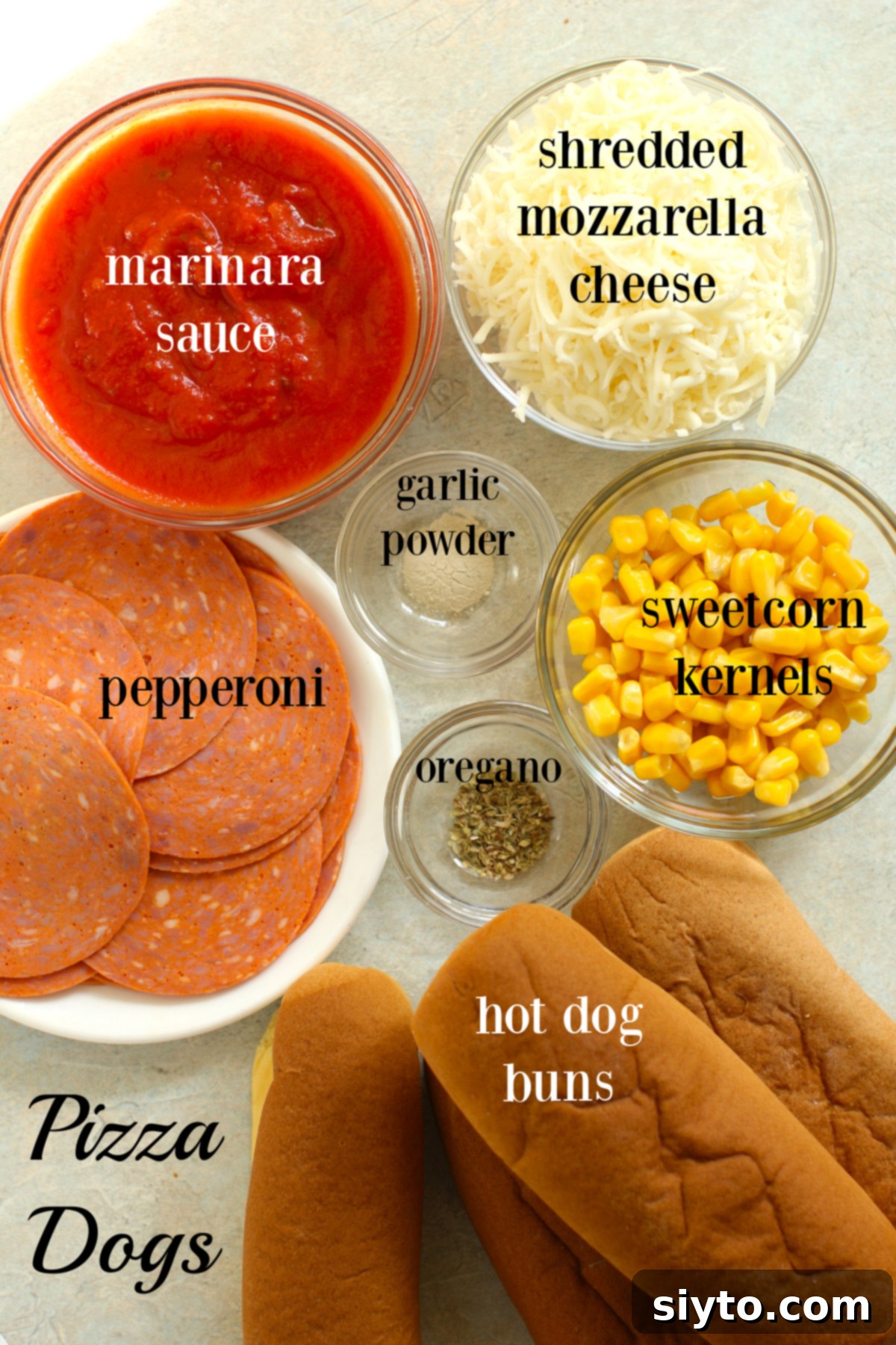 A flat lay of all the essential ingredients for making pizza dogs: hot dog buns, marinara sauce, pepperoni slices, shredded mozzarella cheese, garlic powder, dried oregano, and corn kernels.
