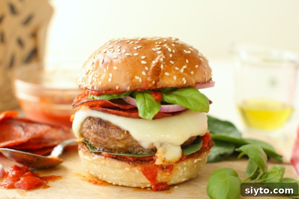 pizza burger with all the fixings, basil sprig beside it, spoon of sauce on the other side.