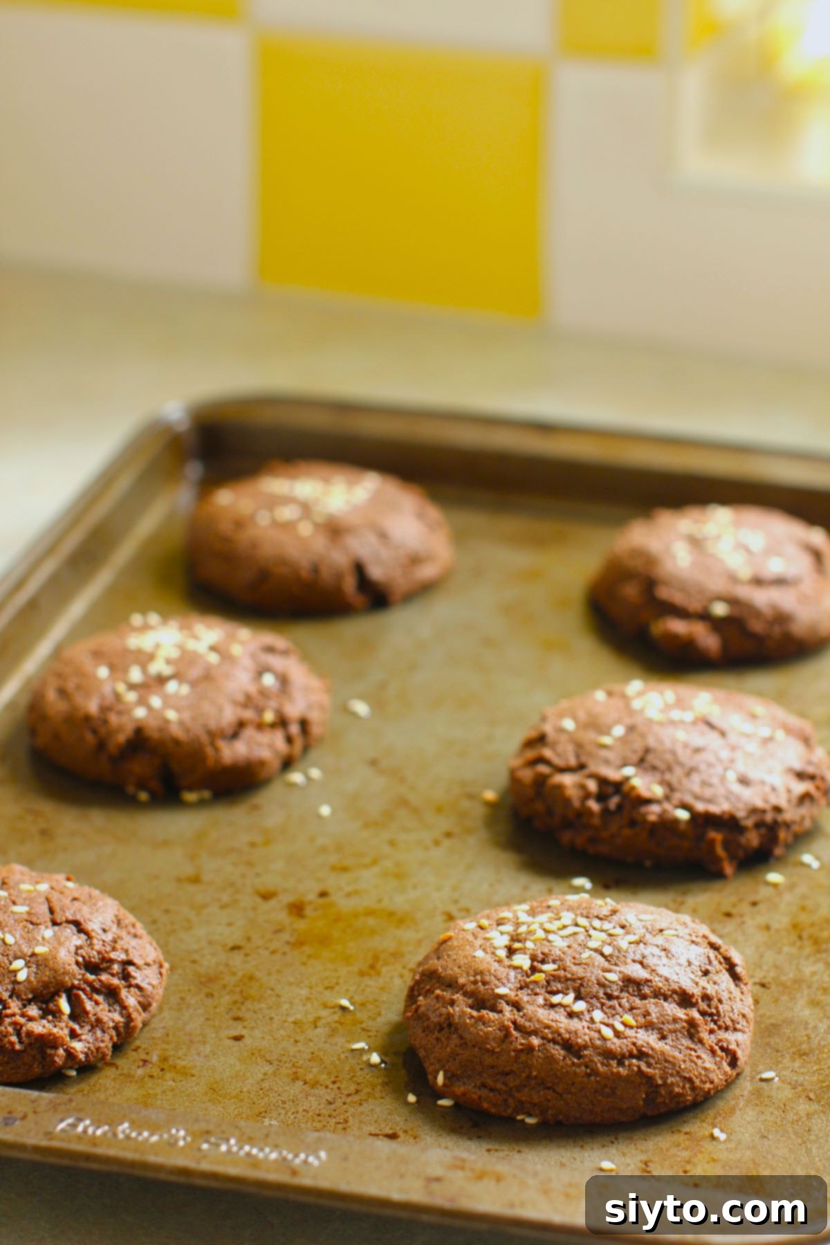 A baking pan filled with freshly baked soft chocolate tahini cookies, just out of the oven, showing their puffed tops and inviting texture.