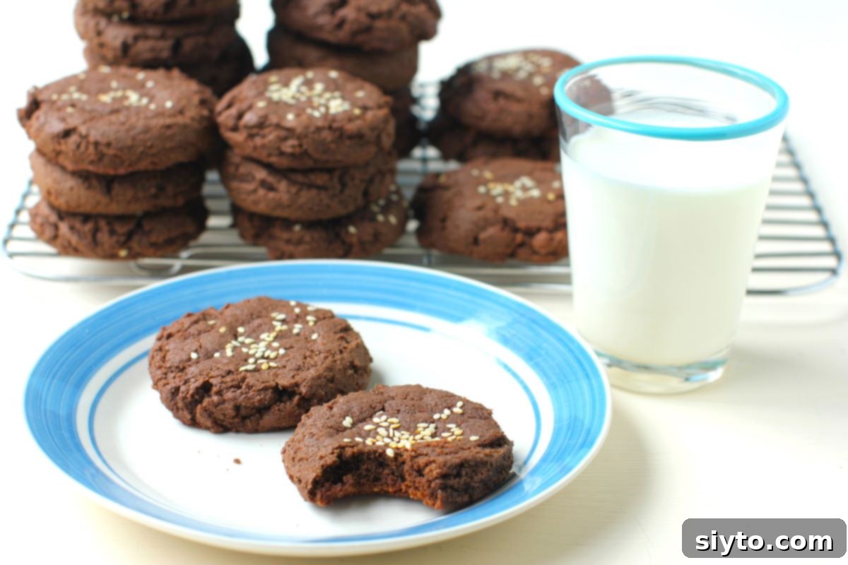 A cooling rack with soft chocolate tahini cookies, next to a plate with two cookies and a glass of milk, inviting a delicious treat.