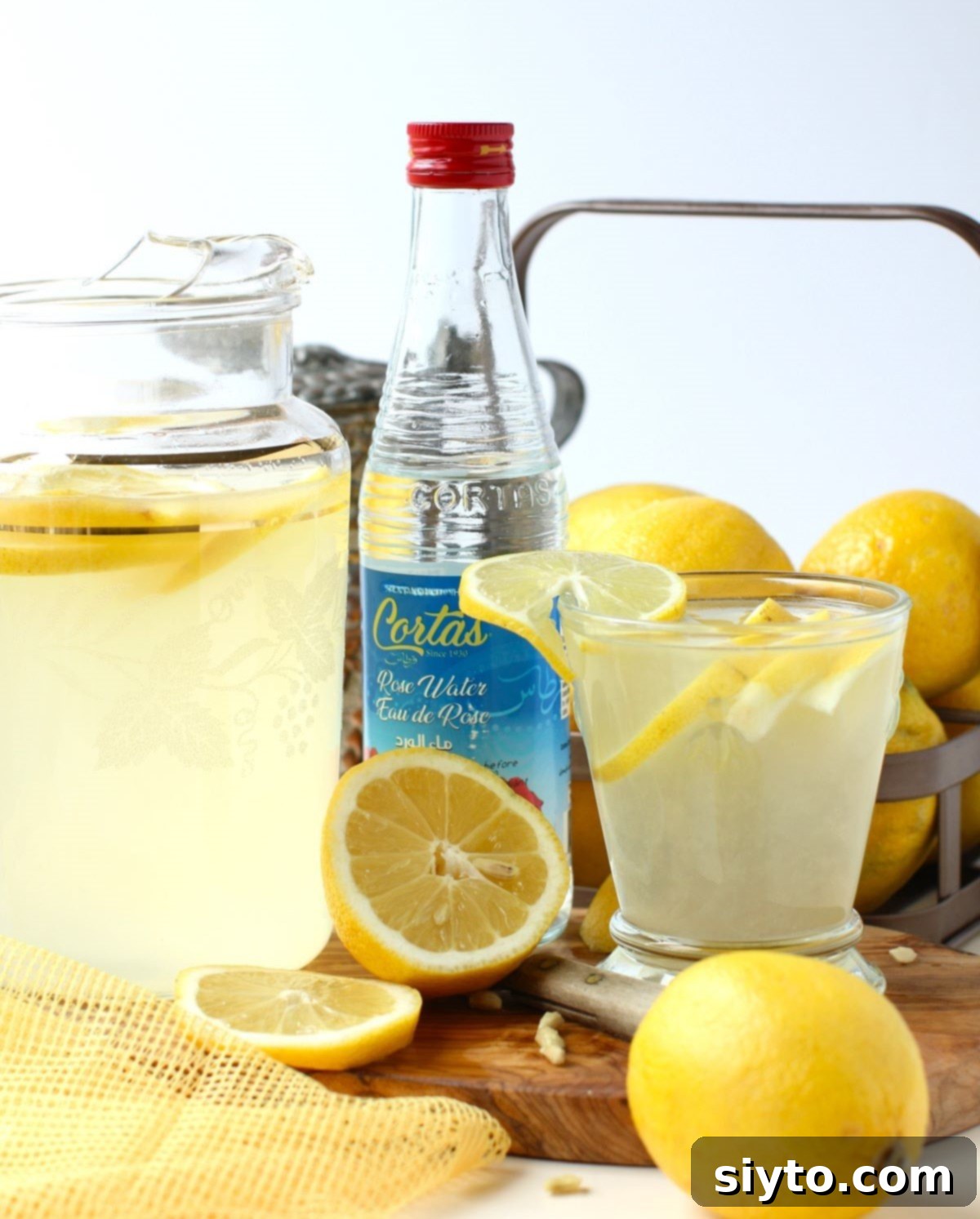 A pitcher of refreshing Omani rosewater lemonade is shown alongside a single glass filled with the drink and a small bottle of pure rosewater, highlighting the key ingredient.