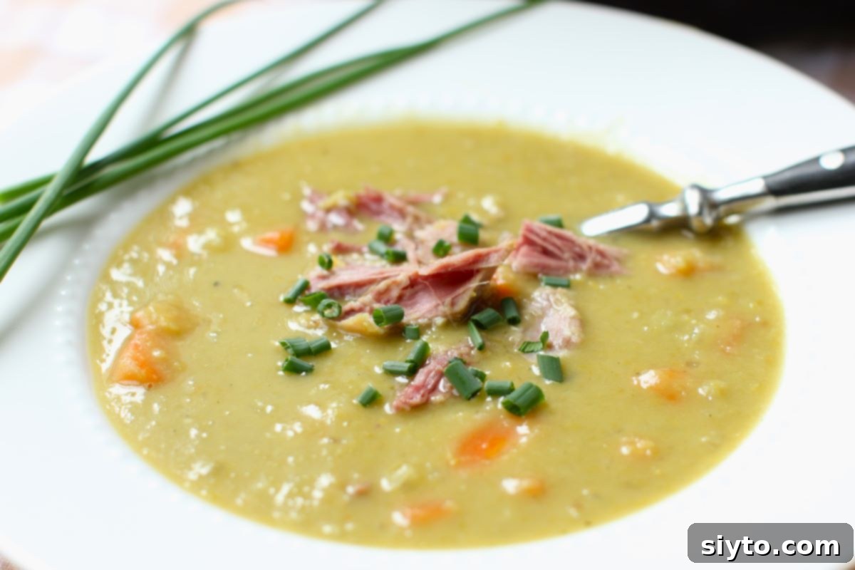 Perfectly Simple Split Pea Soup 9 White rimmed bowl of pea soup with shredded ham and chives on top.