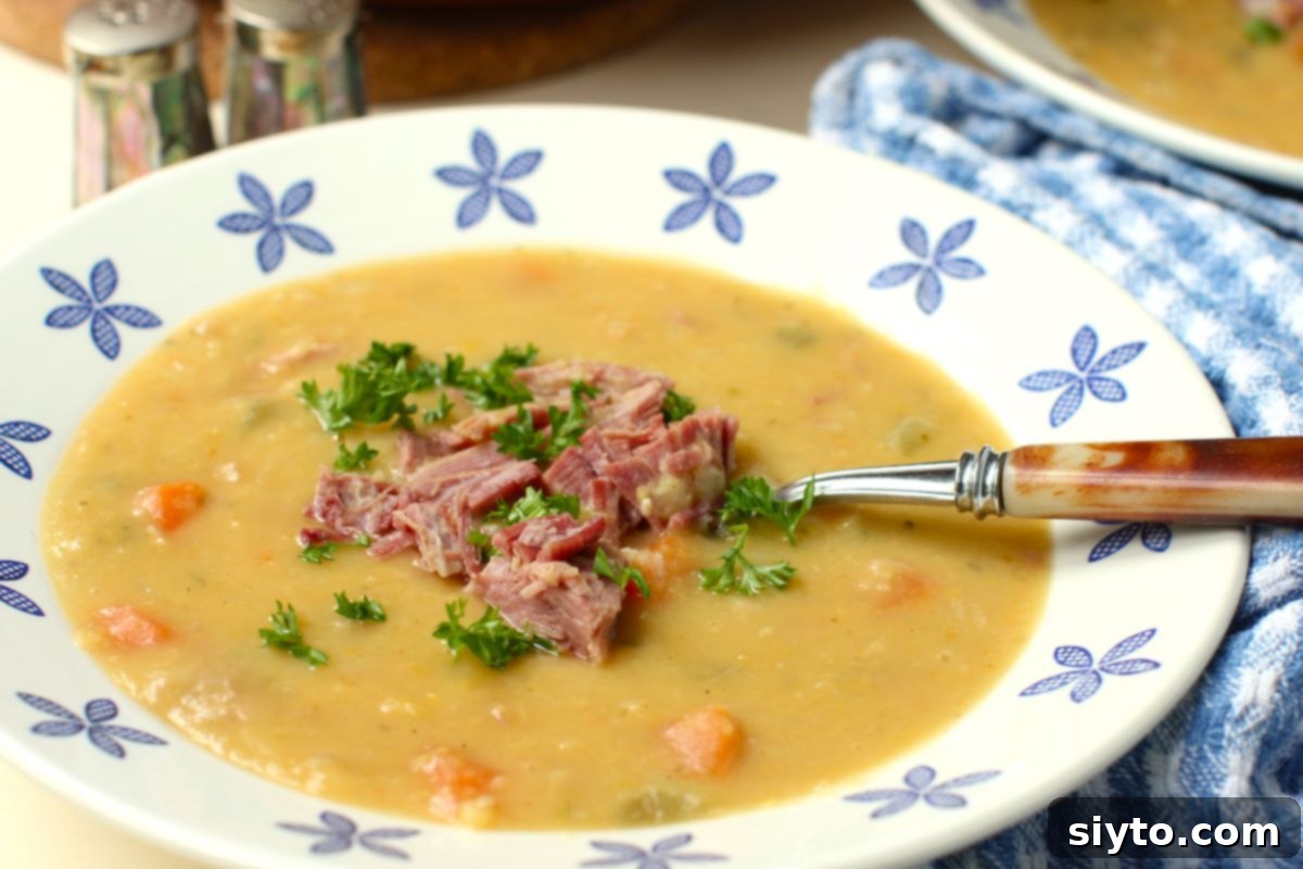 Perfectly Simple Split Pea Soup 10 bowl of soup made with yellow split peas, ham bits in center.