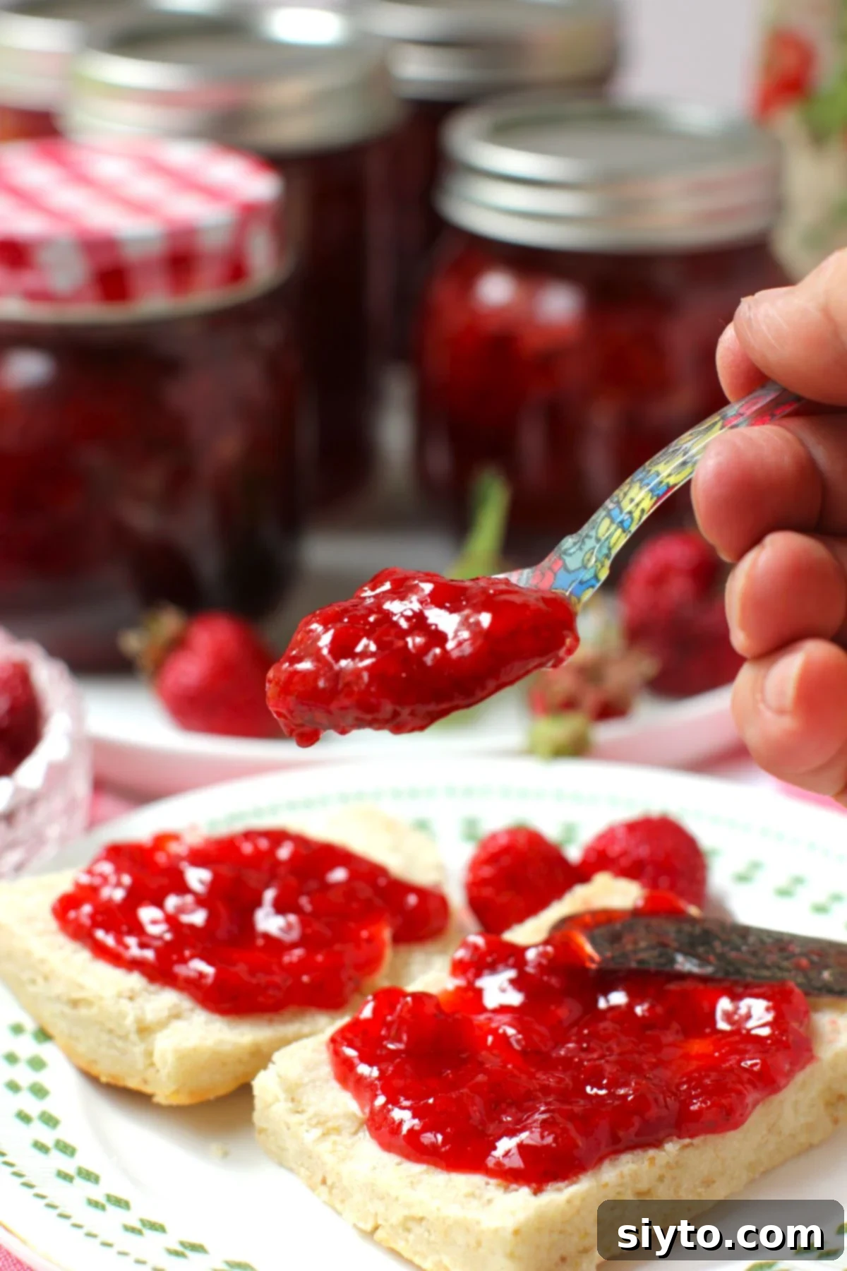 Reduced Sugar Strawberry Jam 4 Holding a spoonful of strawberry jam in front of biscuits spread with it.