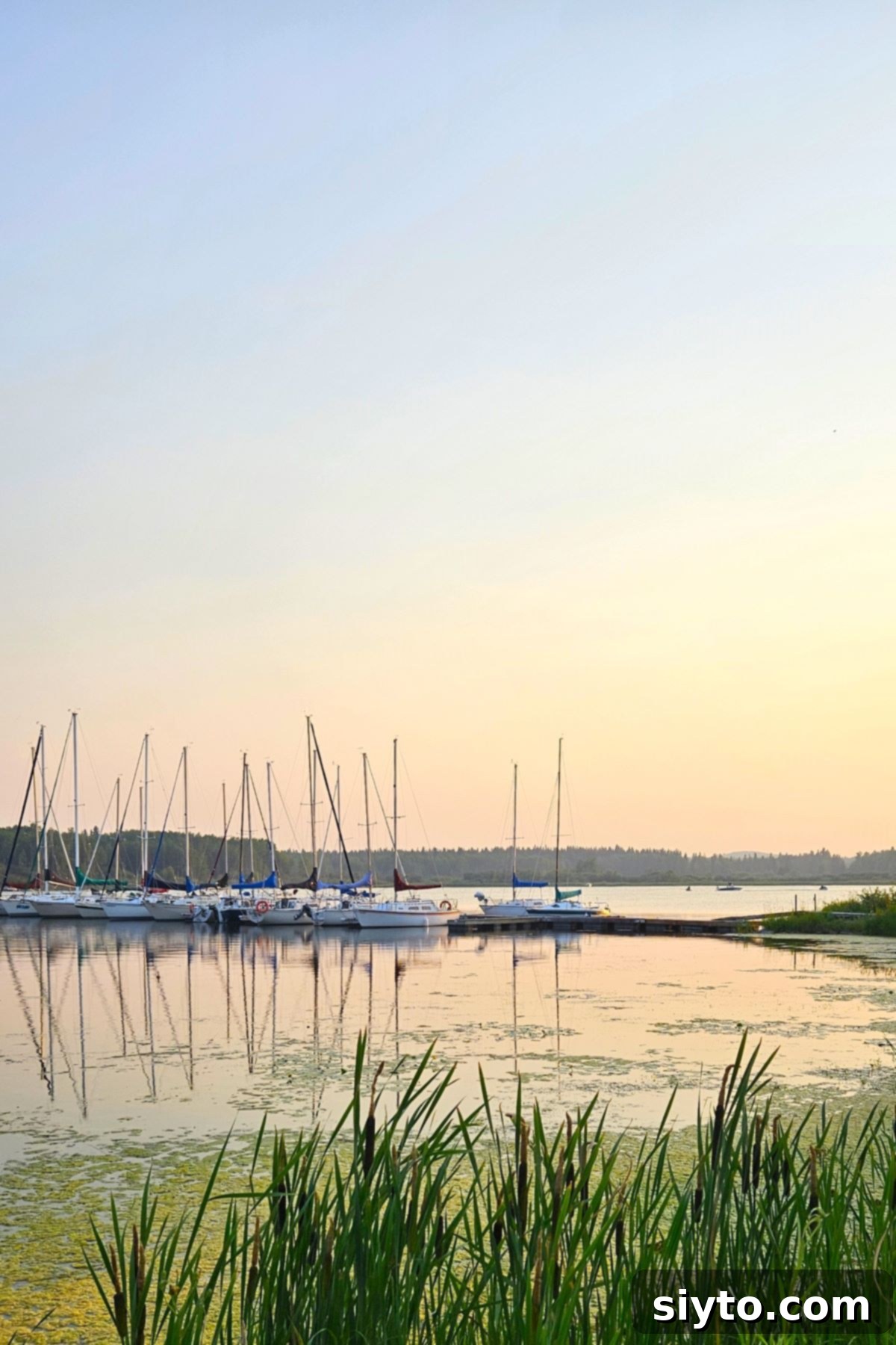 A breathtaking sunset over a lake, with the silhouettes of sailboats docked peacefully against the vibrant orange and purple sky.