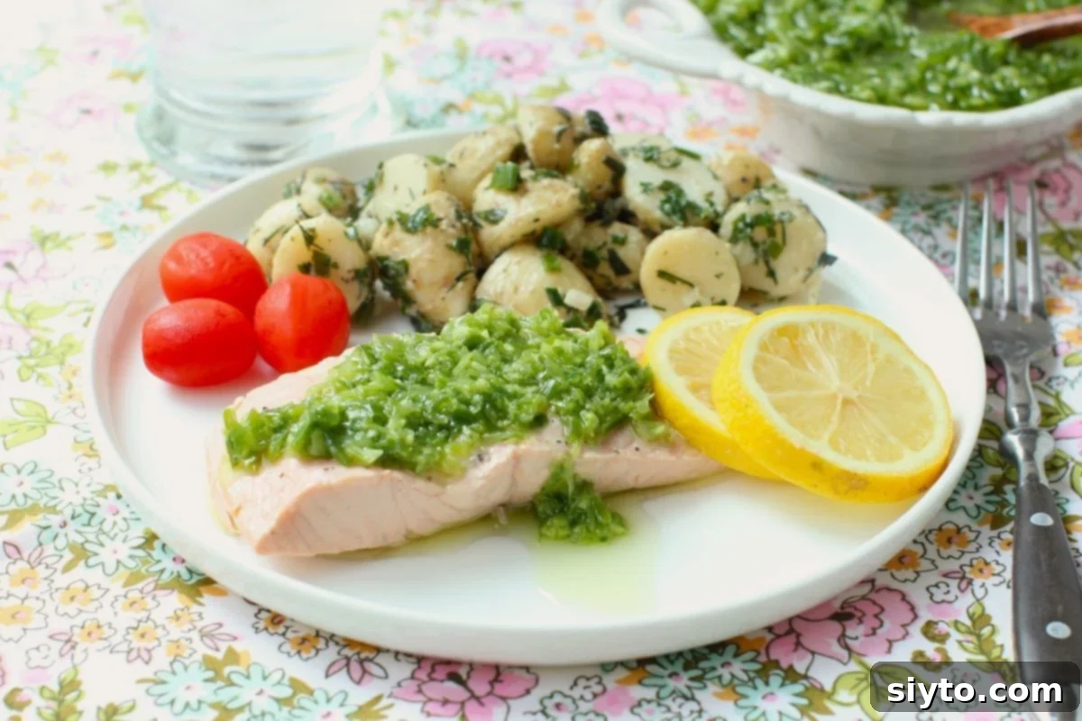 A white plate featuring a piece of cold poached salmon elegantly topped with ginger scallion sauce, served alongside a vibrant potato salad.
