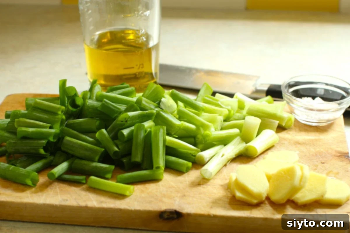 Freshly chopped 1-inch green onion pieces and thinly sliced fresh ginger laid out on a clean cutting board, ready for processing.