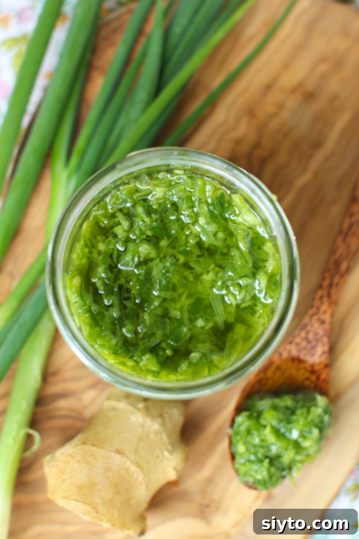A top-down view looking into an open glass jar, showing the vibrant green and golden texture of homemade ginger scallion sauce.