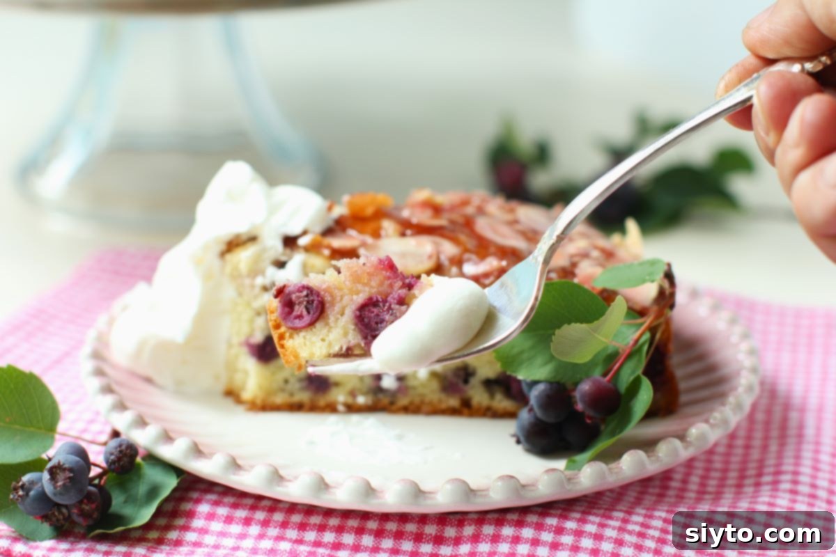Saskatoon Berry Drizzle Cake 13 A fork lifts a tender bite of Saskatoon Drizzle Cake, showcasing the moist crumb and visible saskatoon berries, with a glazed slice of the cake resting on a plate in the softly blurred background.