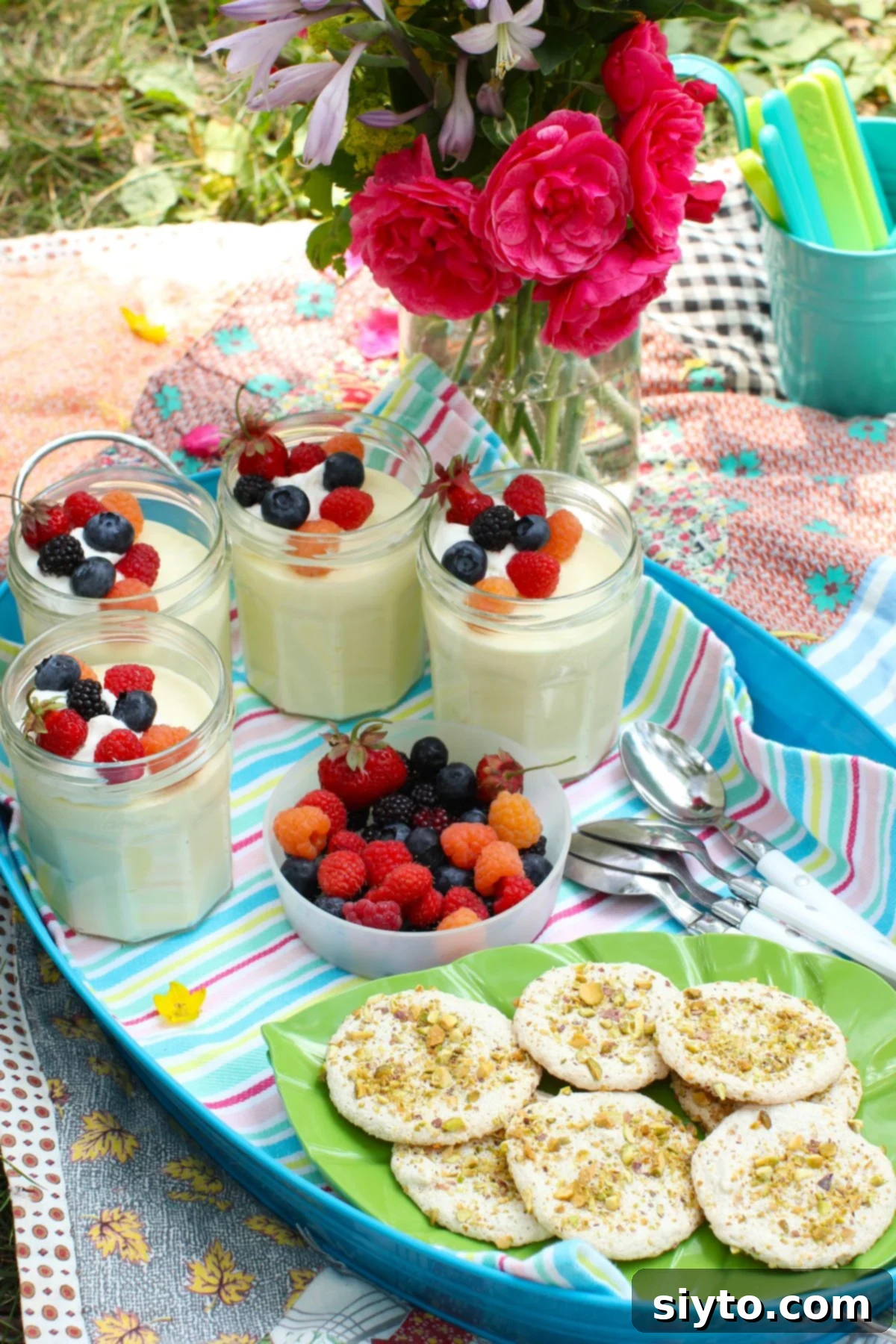 Delightful lemon mousse in individual jars, topped with fresh berries, arranged on a blue tray beside a bowl of extra berries and a plate of cookies for a picnic.