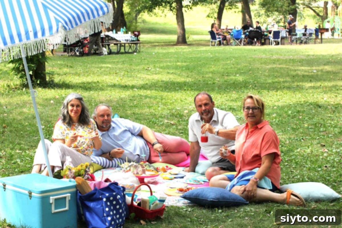 A candid photo of four friends – Nicoletta, Loreto, Raymond, and Margaret – happily sitting together on a colorful picnic blanket, enjoying their outdoor time.