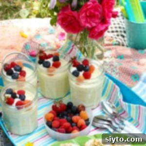 Four jars of light and tangy lemon mousse, elegantly topped with fresh mixed berries, arranged on a blue serving tray next to a bowl of extra berries and a plate of crunchy cookies.