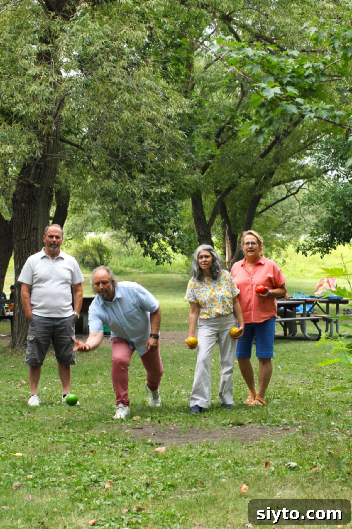Four people are actively engaged in a game of bocce ball on the grass, enjoying the outdoor picnic activities.