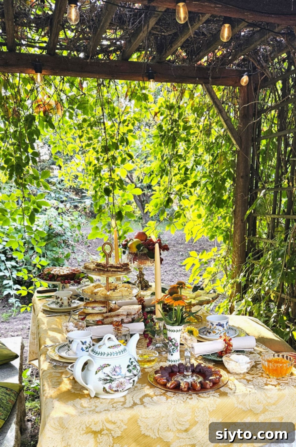 An elegantly set afternoon tea table nestled under a cedar arbour, adorned with delicate string lights.