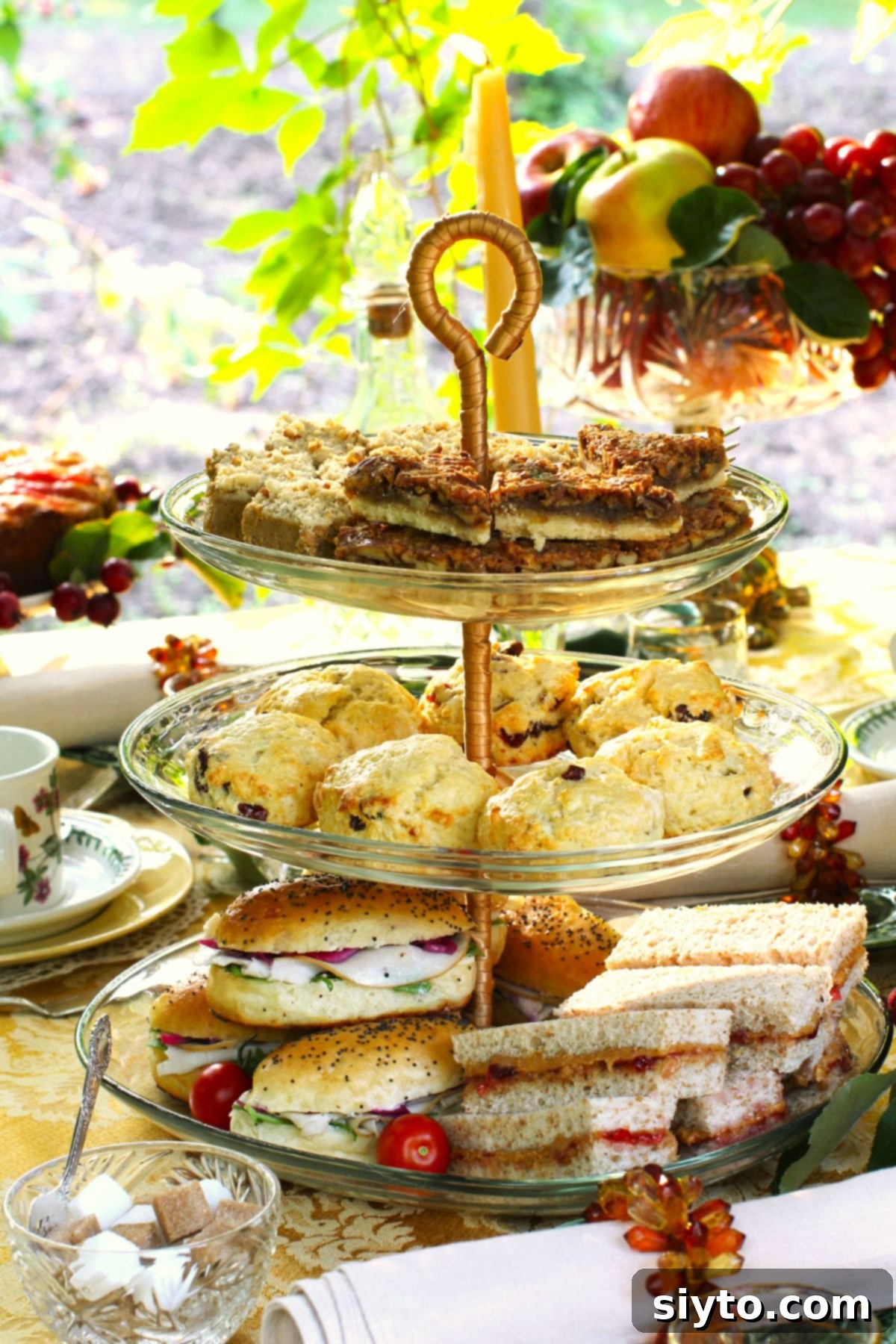 A meticulously arranged 3-tiered stand on the tea table, featuring Butter Pecan Bars prominently on the top, warm scones in the middle, and savory sandwiches on the bottom tier.