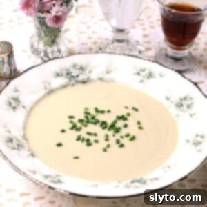 Rimmed china soup bowl with cream of puffball soup garnished with a scattering of chopped chives.