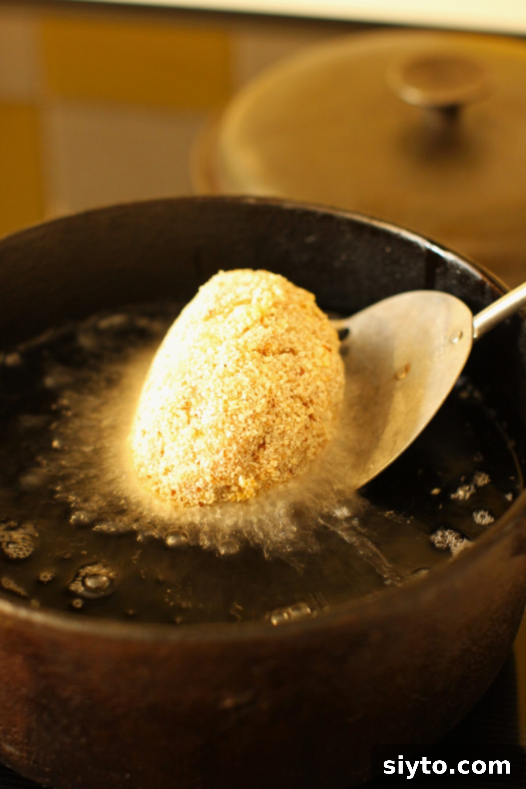 Lowering a Scotch egg into the hot oil with a slotted spoon.