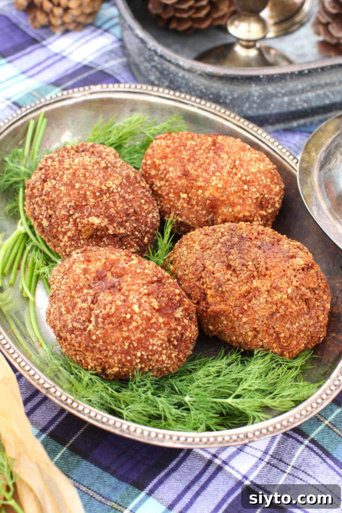 4 Scotch eggs on a silver platter, surrounded by sprigs of fresh dill.