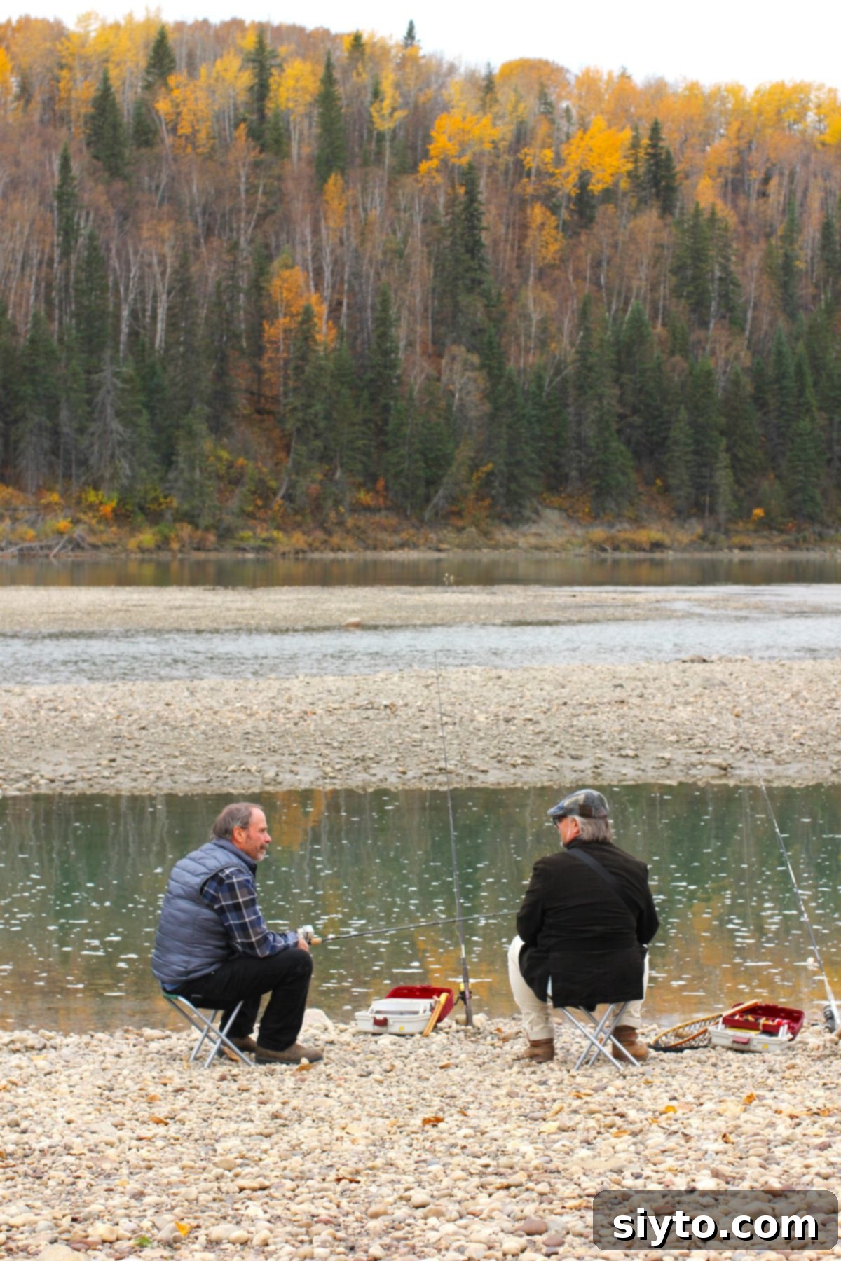 Two guys sitting on stools on the river banks, fishing.