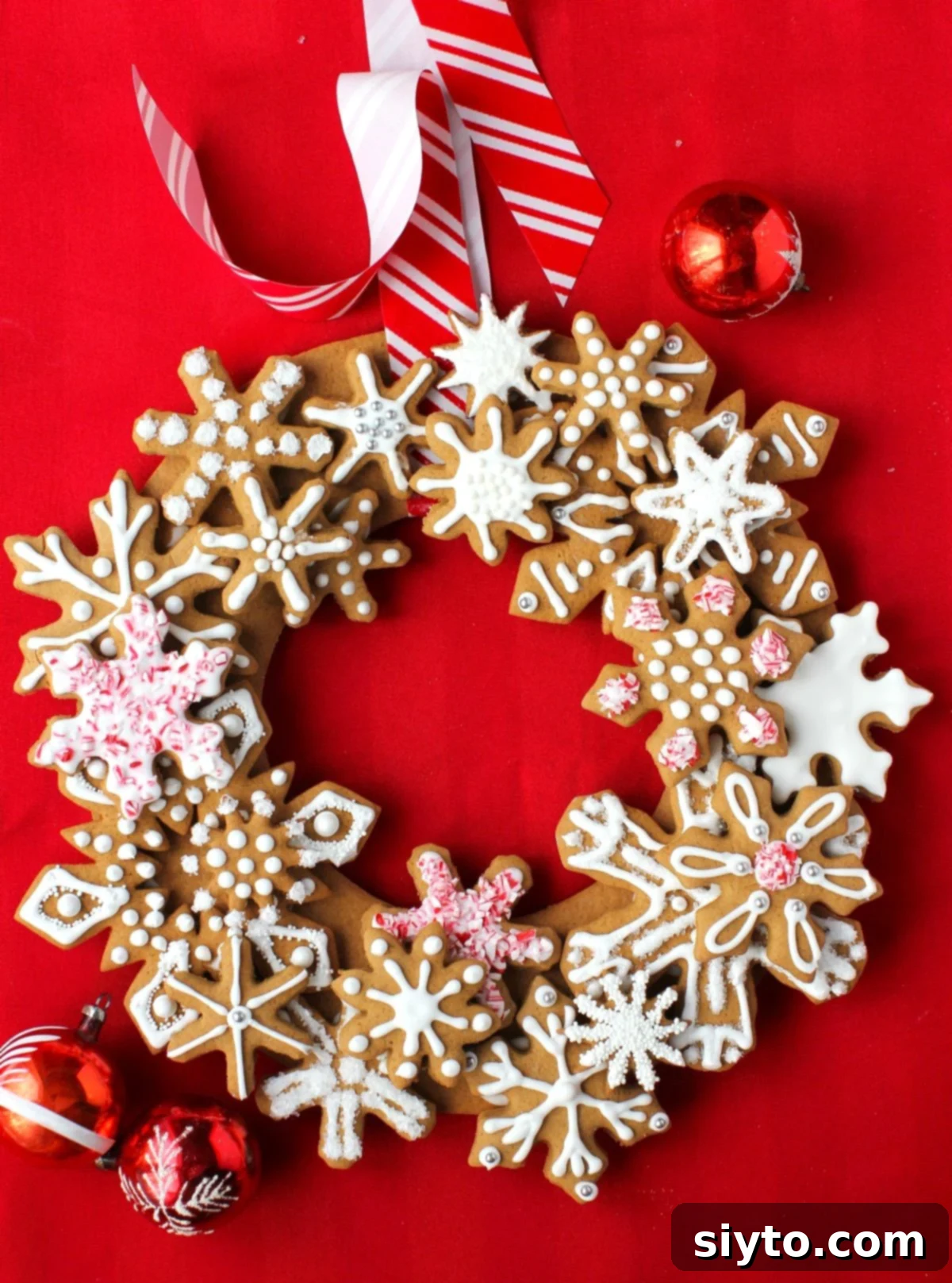 Iced Gingerbread Snowflake Cookie Wreath on a red background, with red glass ornament balls. A beautiful edible decoration for Christmas.