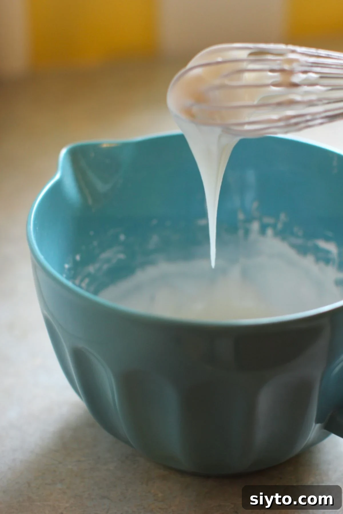 Holding up a whisk full of royal icing, dripping off in a thick triangle, illustrating the ideal consistency for piping detailed decorations.