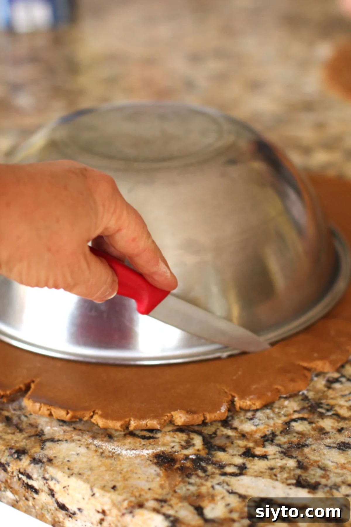 Cutting around the outside of a big bowl laid on the rolled out gingerbread cookie dough to make the outside of the wreath shape, using a sharp knife.