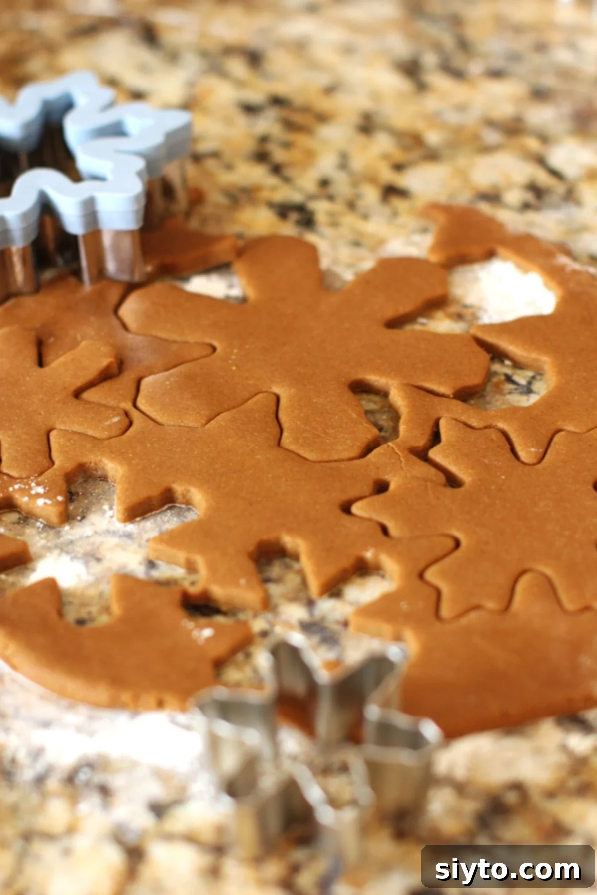 Cutting out snowflake shapes from the gingerbread cookie dough with various cookie cutters.