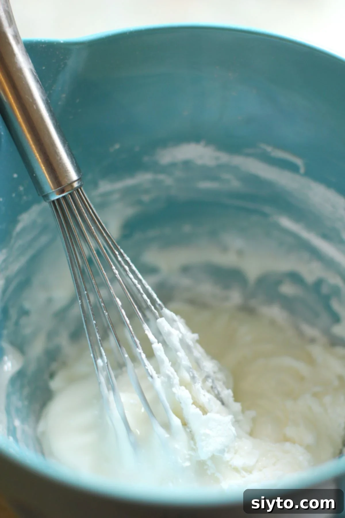 Making royal icing in a blue bowl with a whisk, showing the initial mixing stage.