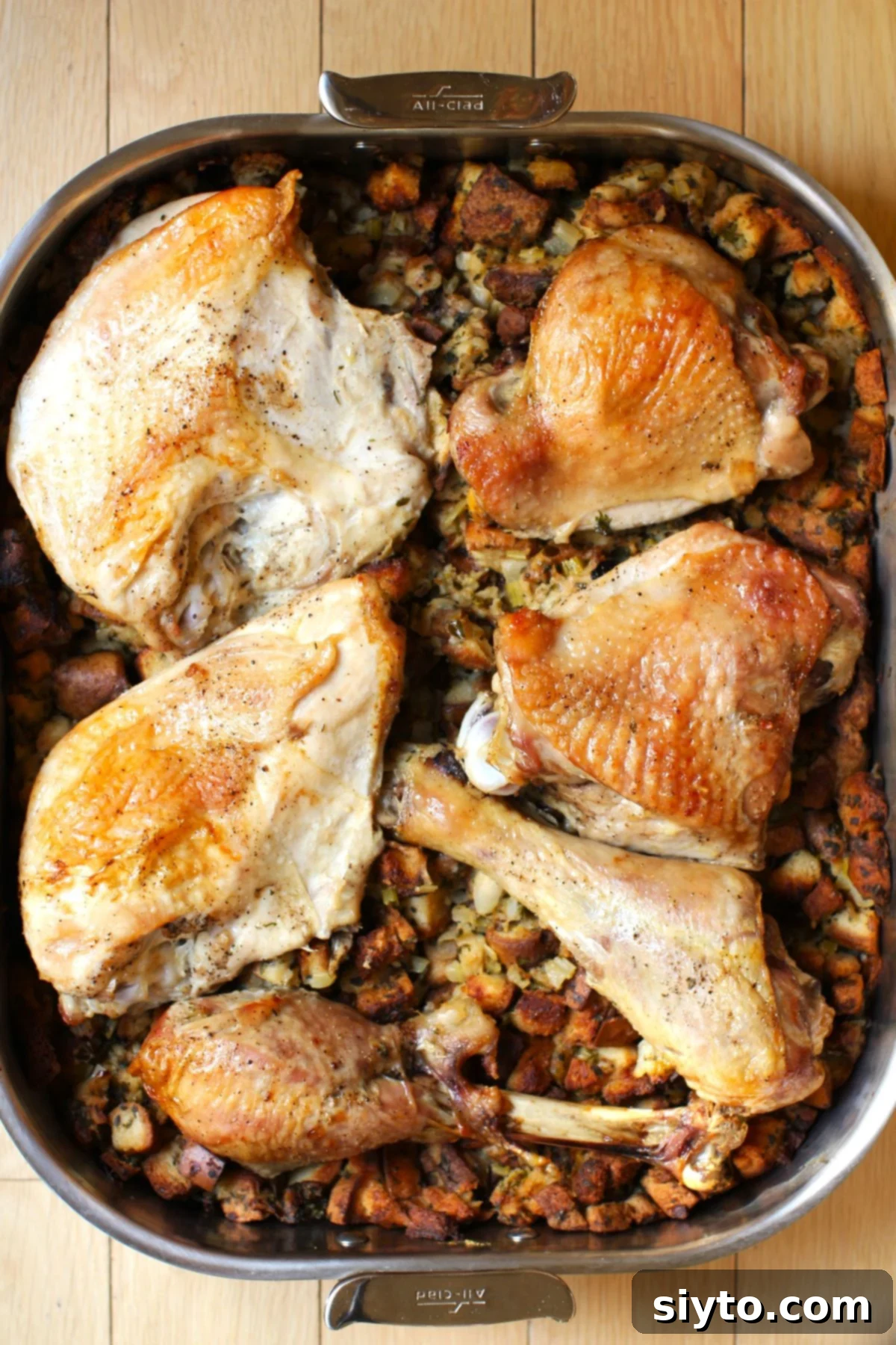 A large roasting pan filled with golden-brown, perfectly roasted turkey pieces nestled atop a generous layer of savory stuffing. The skin is crisp, and the stuffing has deliciously browned edges.