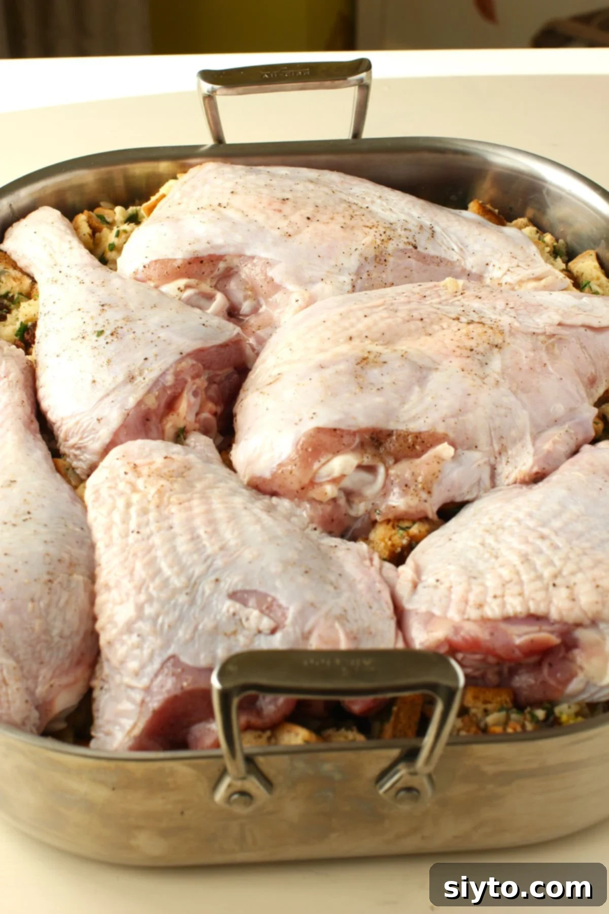 A prepared roasting pan, filled with stuffing and topped with seasoned turkey pieces, ready to be put into the hot oven for roasting.