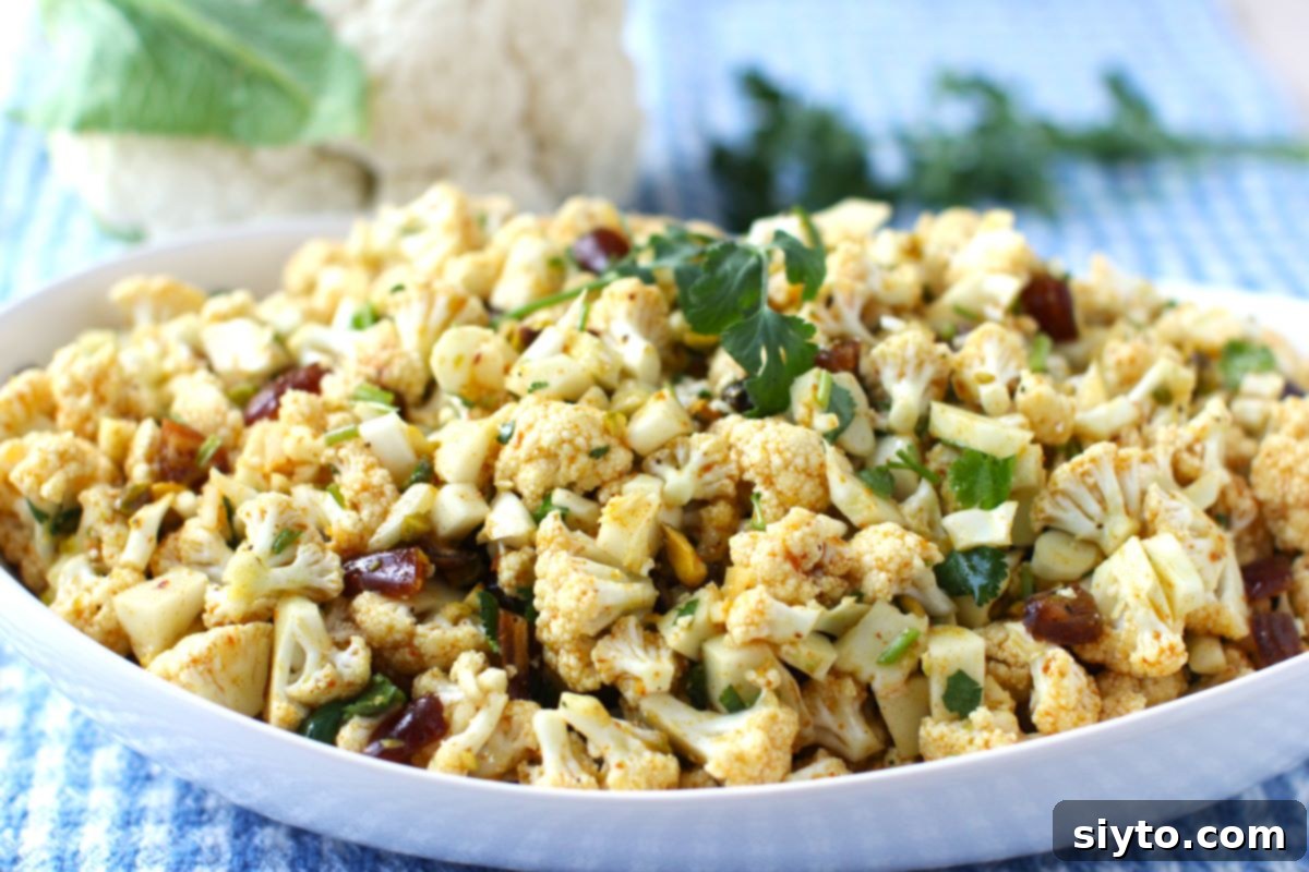 Horizontal view of bowl of cauliflower, date & pistachio salad with heat of cauliflower behind.