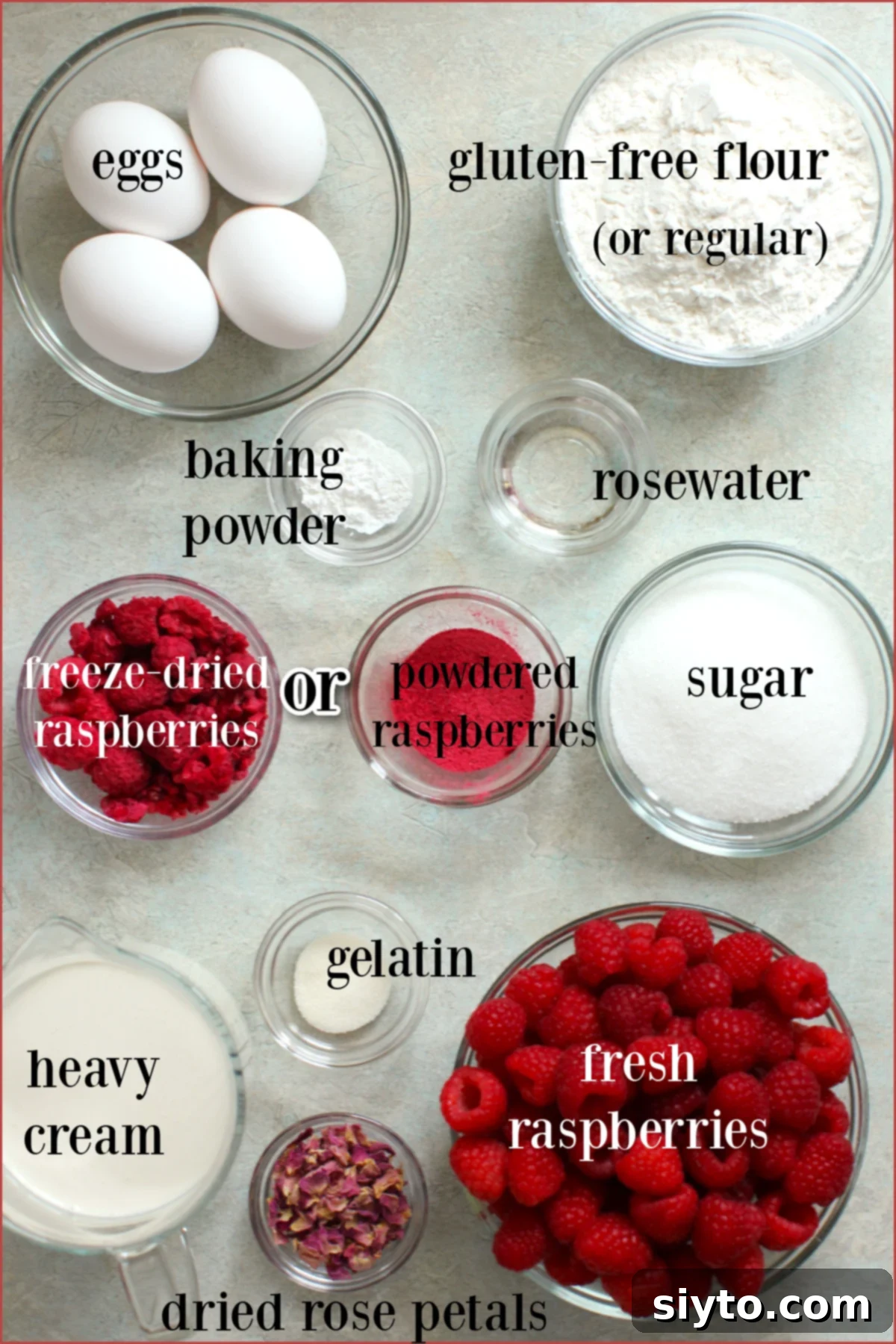 Bowls of neatly arranged ingredients for Raspberry Rose Heart Cake on a counter, including fresh raspberries, flour, raspberry powder, rosewater, gelatin, and sugar, all ready for baking.