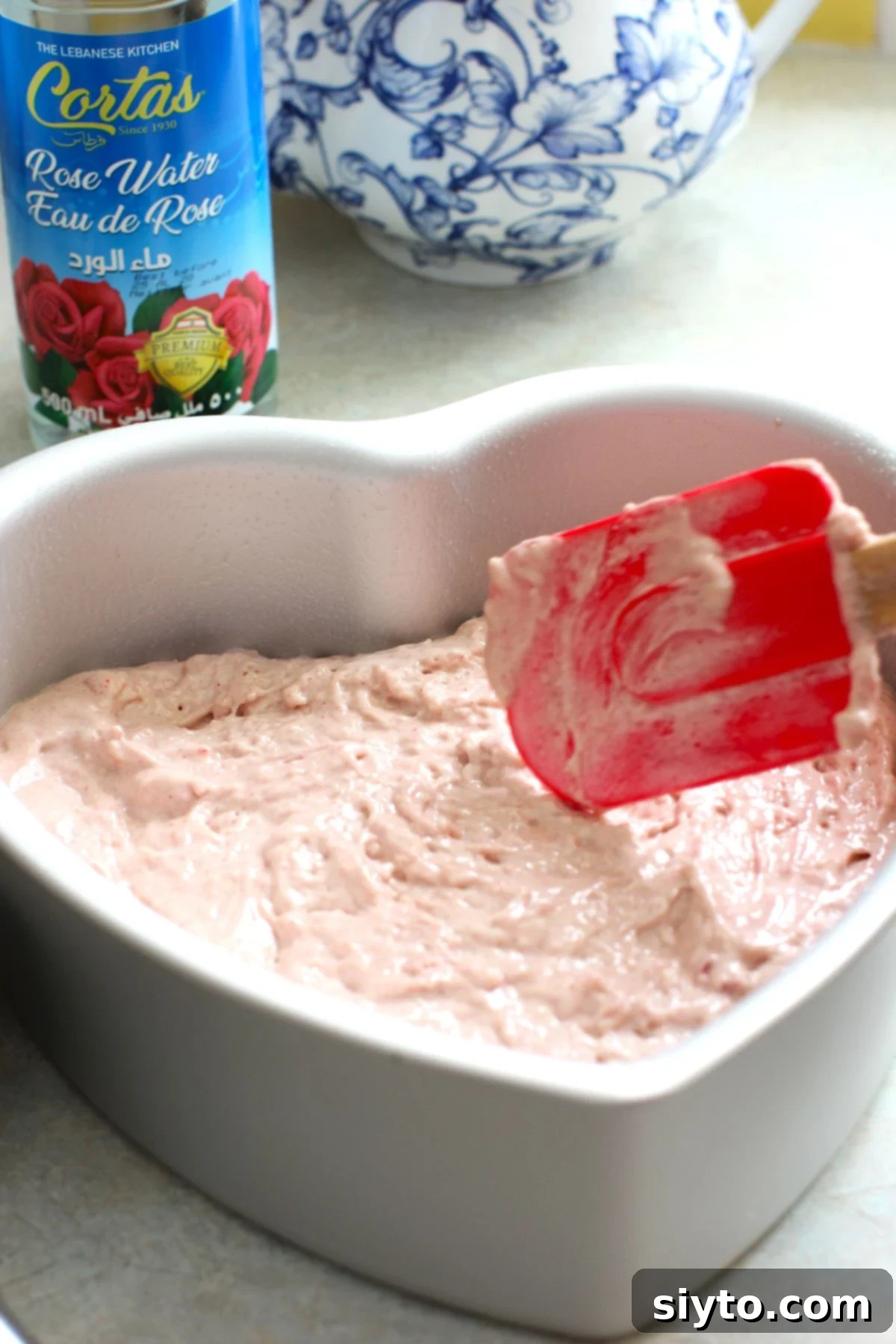 Cake batter being smoothly leveled in a heart-shaped baking pan lined with parchment paper, ready for the oven to bake into the Raspberry Rose Heart Cake.