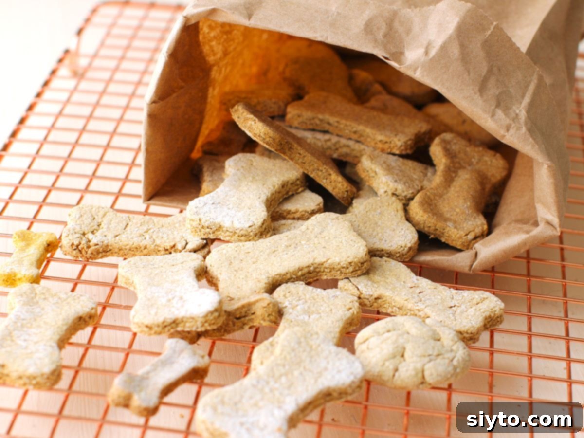 Horizontal photo showing a cascade of bone-shaped homemade dog treats pouring out of a rustic paper bag onto a metal cooling rack.