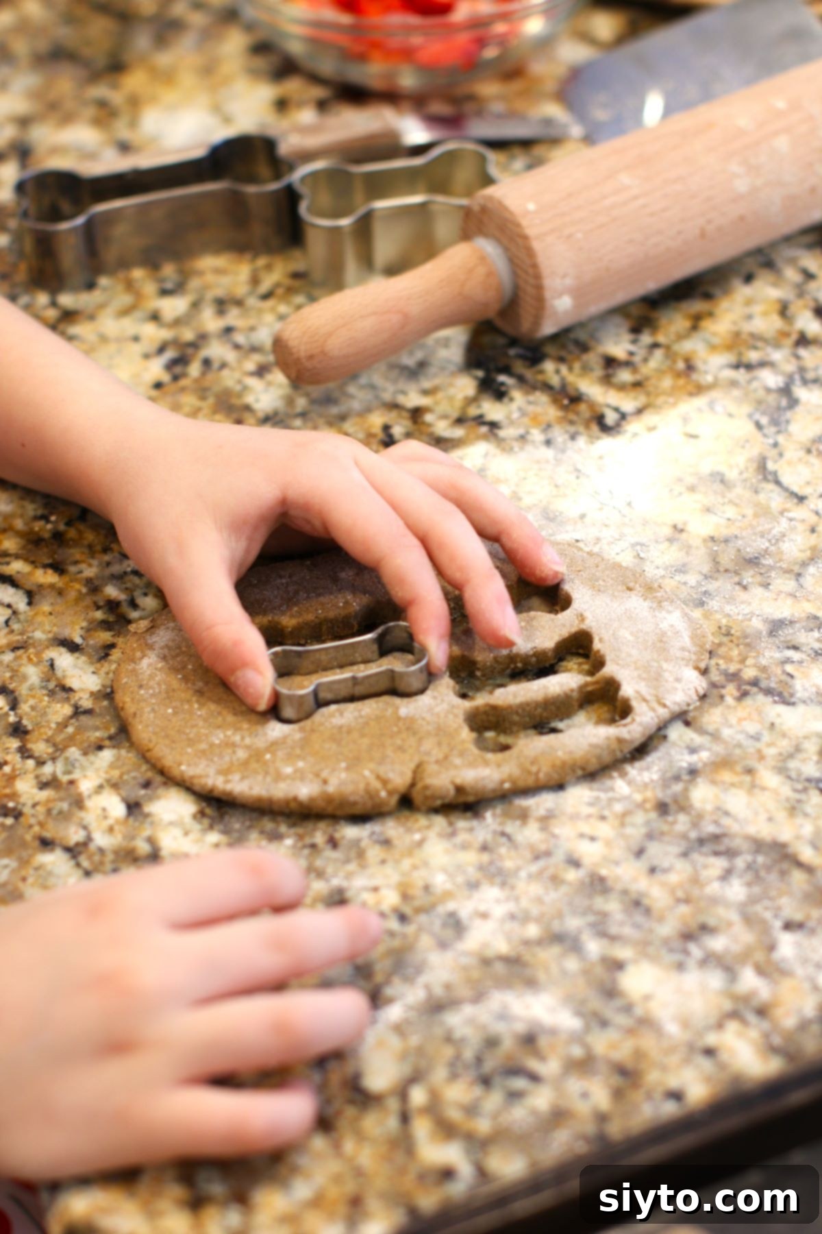 A pair of hands using a bone-shaped cookie cutter to neatly cut out biscuits from the uniformly rolled dough.