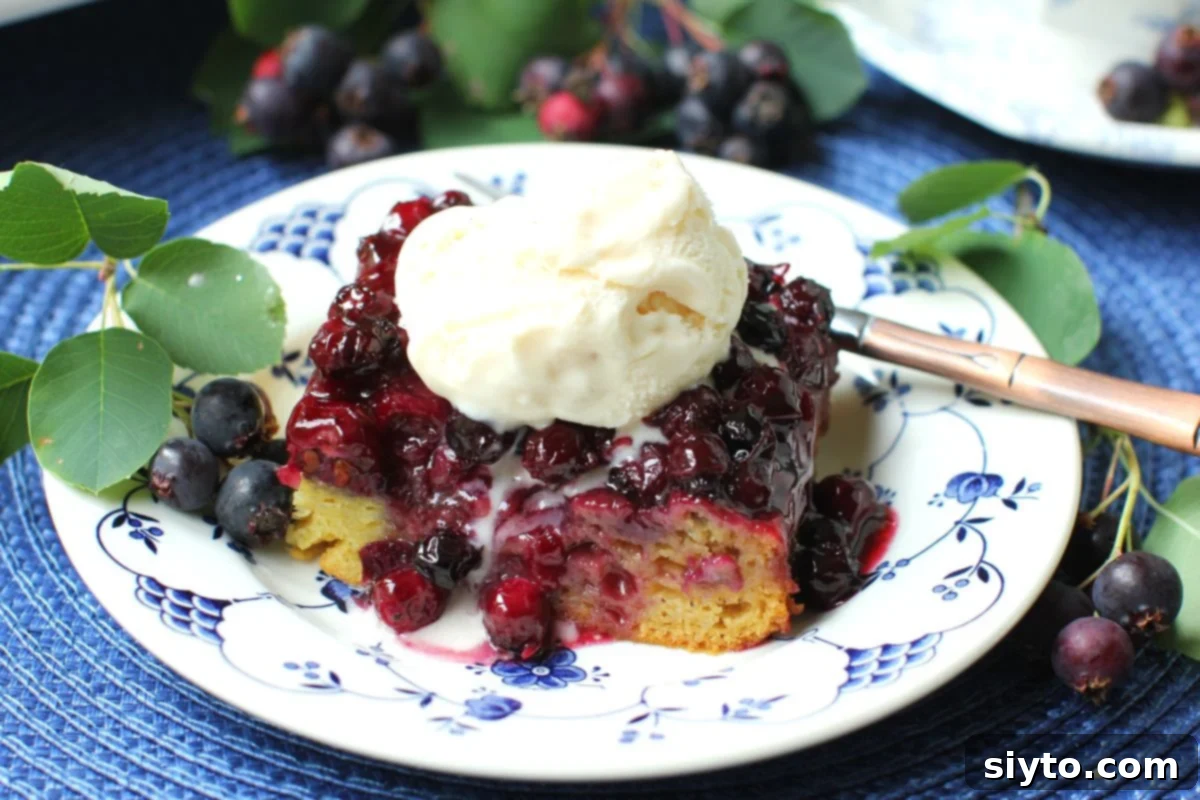 A sqare of saskatoon upside down cake with a scoop of vanilla ice cream melting on top of it.