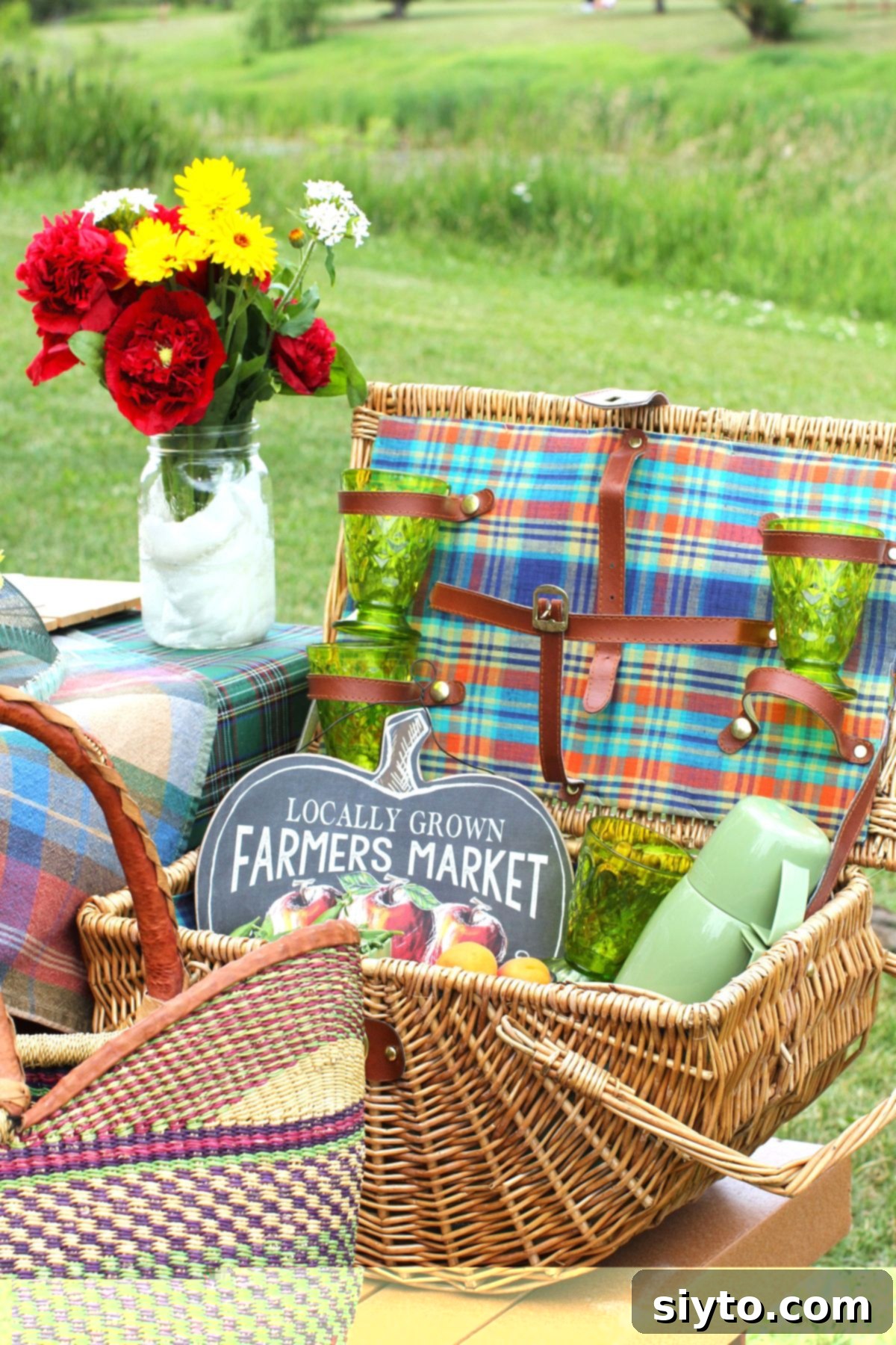 A rustic picnic basket adorned with a small farmers' market sign, positioned in front of a delicate vase of freshly picked flowers.