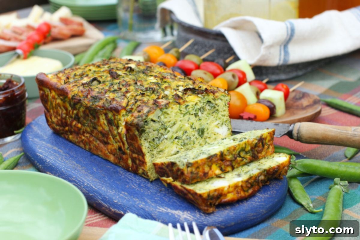 A golden-brown zucchini frittata loaf, partially sliced to reveal its vibrant green and yellow interior, rests on a rustic blue cutting board.