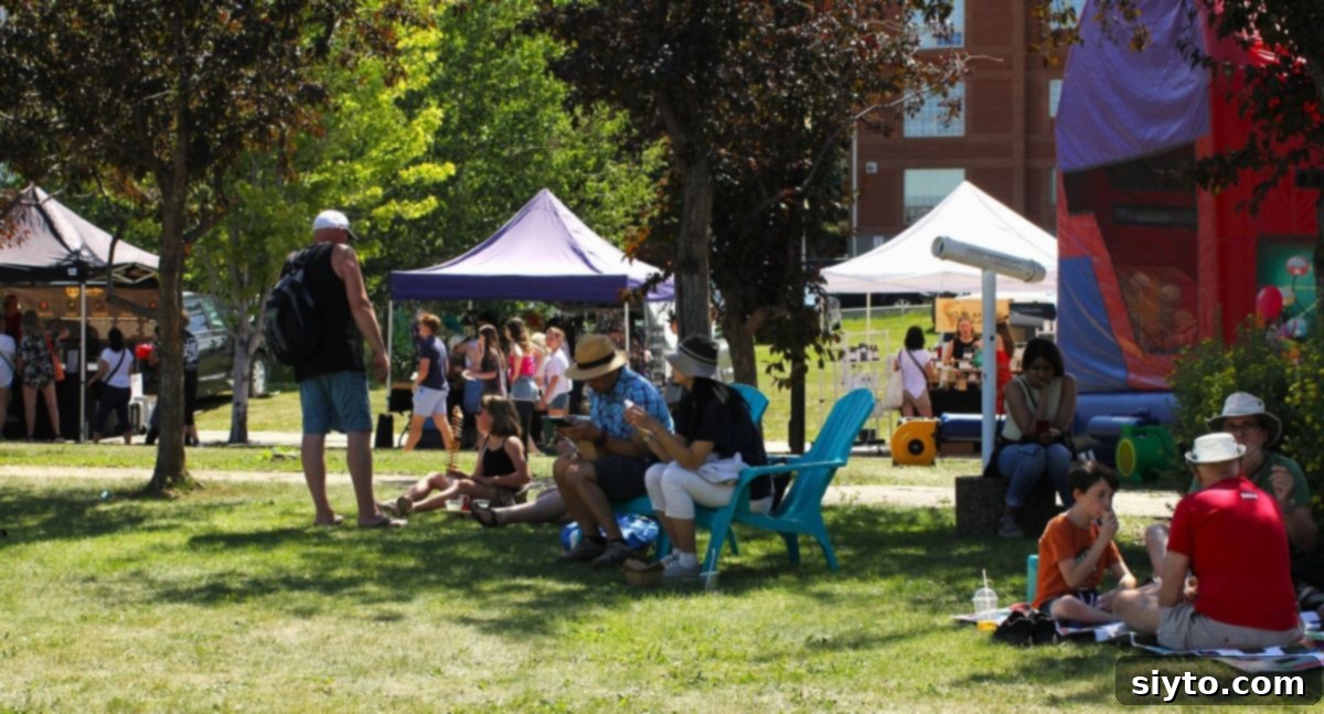 A lush grassy area within the St. Albert Farmers' Market, dotted with market-goers relaxing and enjoying impromptu picnics on a sunny day.