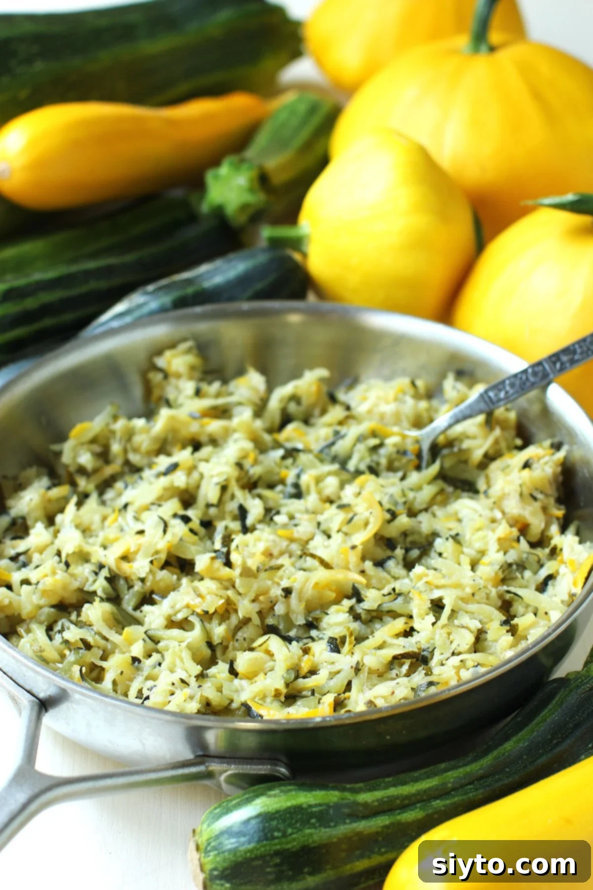 Velvety Zucchini Butter 2 Pan of sauteed shredded zucchini butter with fresh green and yellow zucchini behind it.