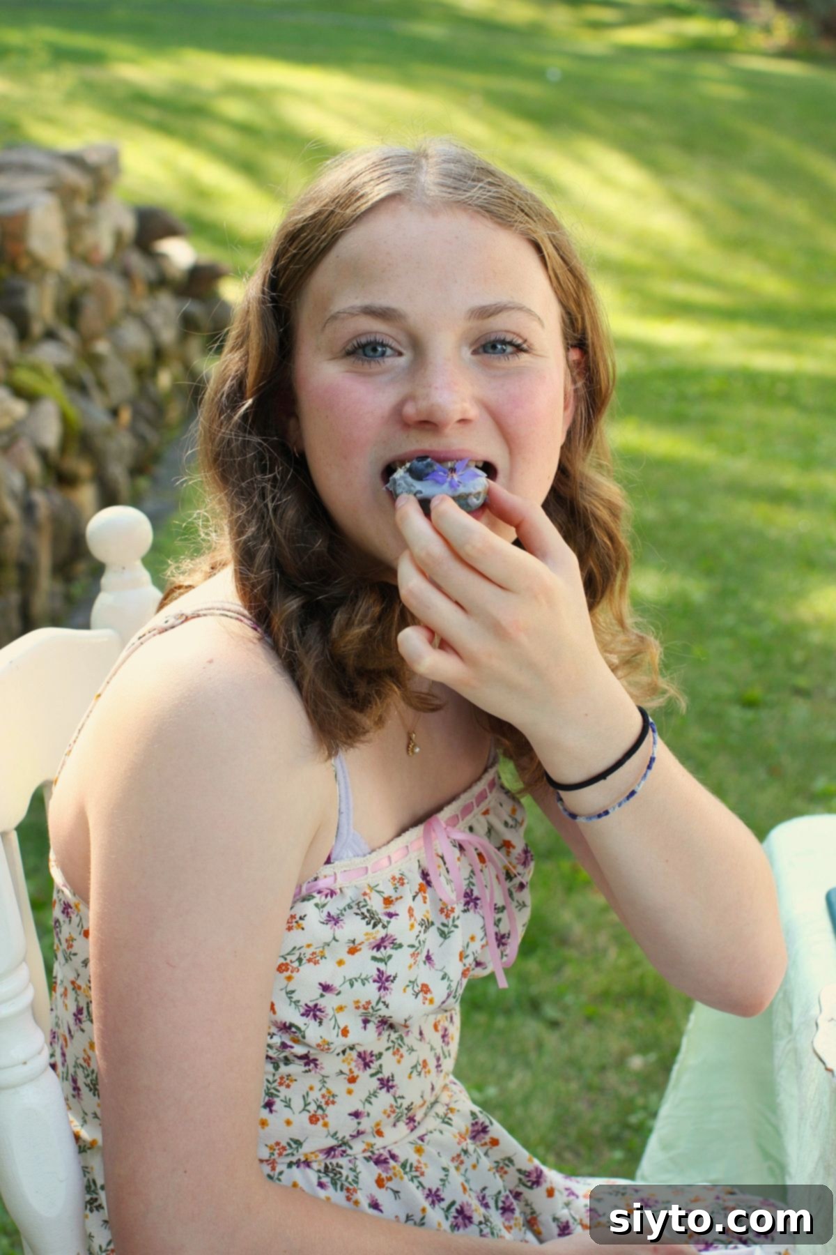 Amelia happily taking a bite out of a mini blue donut, clearly enjoying its delicious taste.