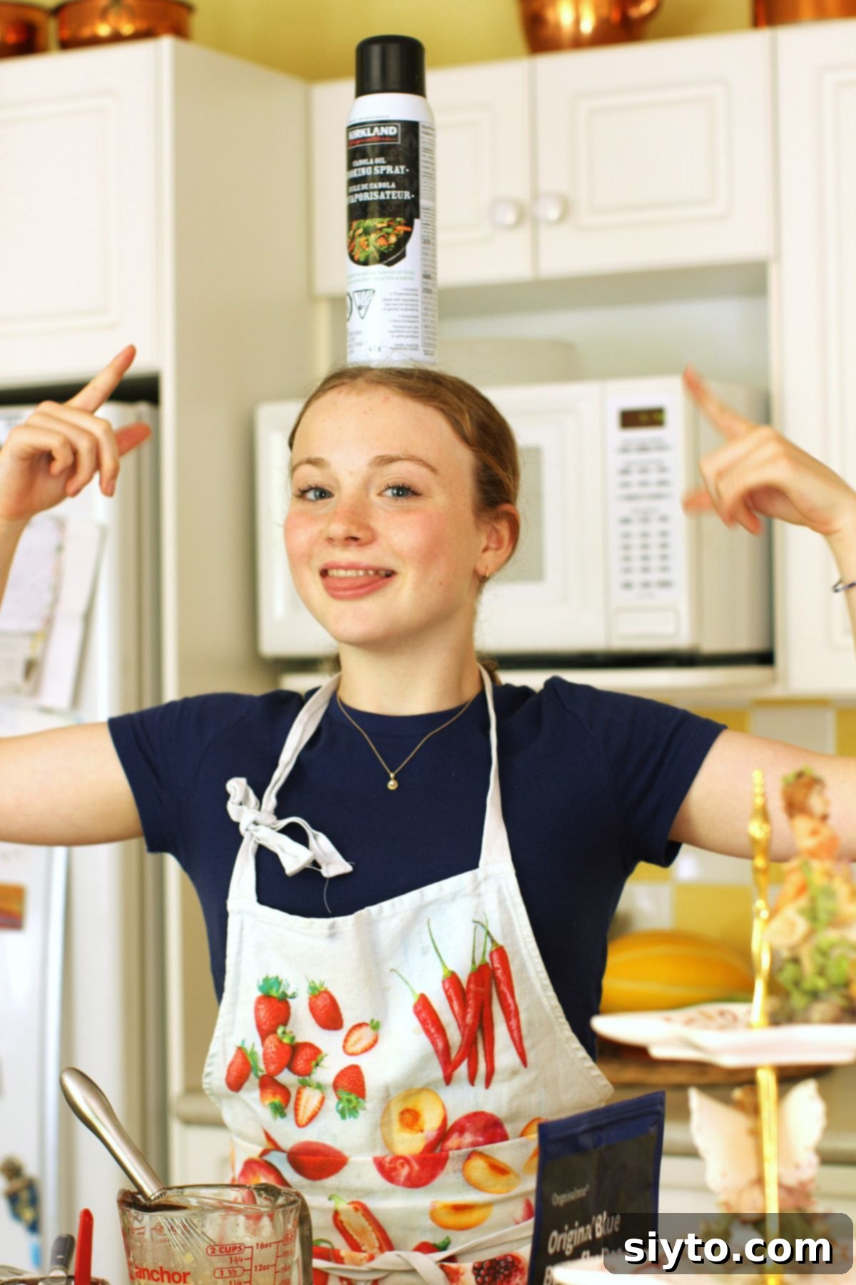 Amelia playfully balancing a can of baking spray on her head, smiling and making light of the baking process.