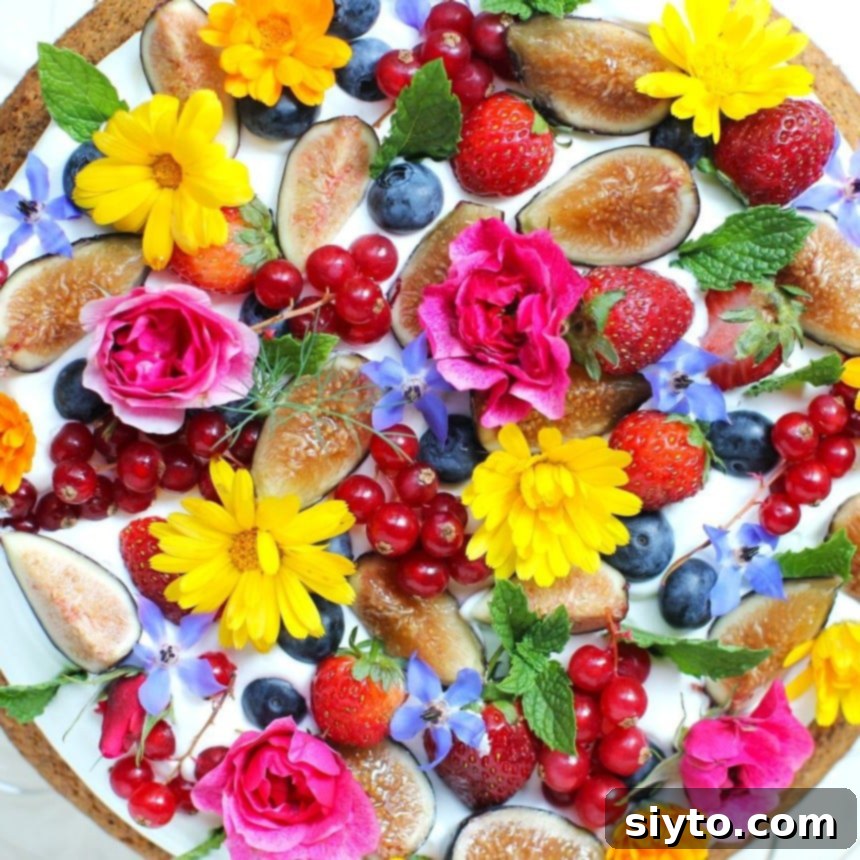 Top view of Fruit & Flower Almond Cake with figs, blueberries, strawberries, red curants, roses, calendulas, borage flowers, and mint leaves;